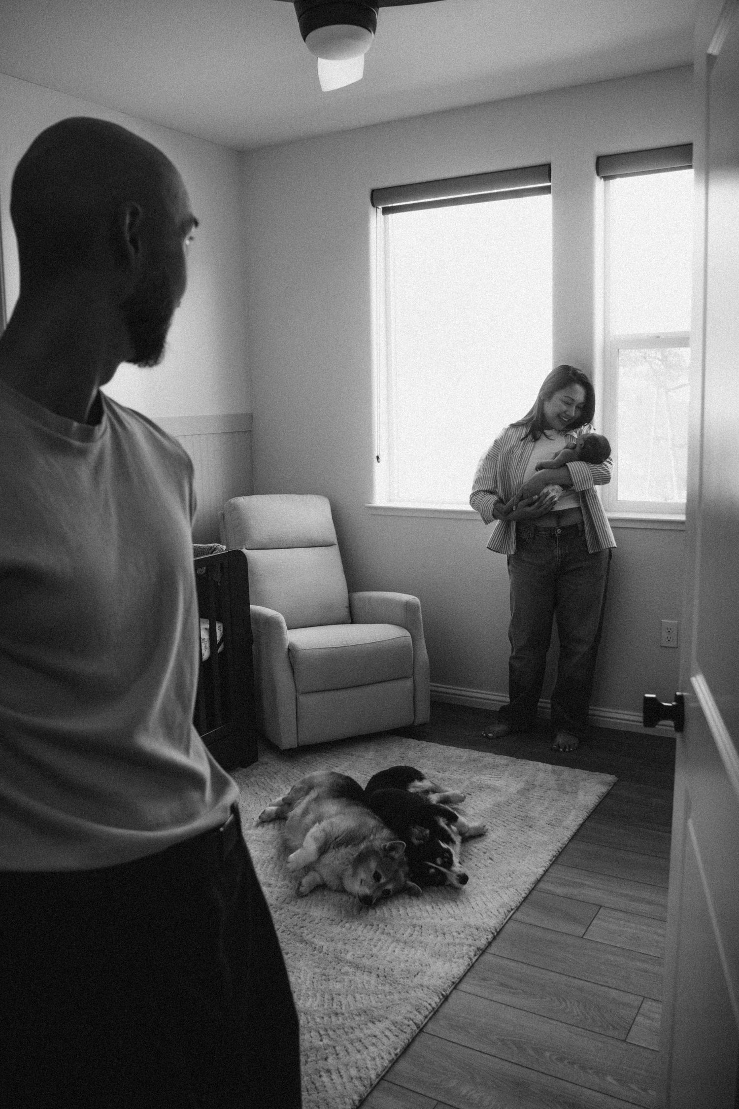 A black and white photo of people in a room with a cat sleeping on a rug near a window.