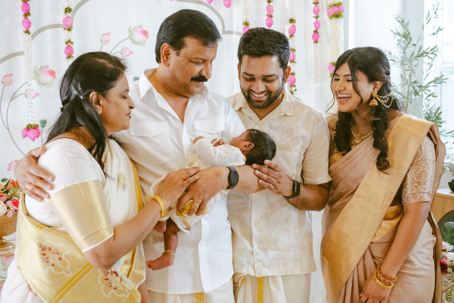 Family gathering celebrating a newborn baby in traditional South Indian attire with floral decorations.