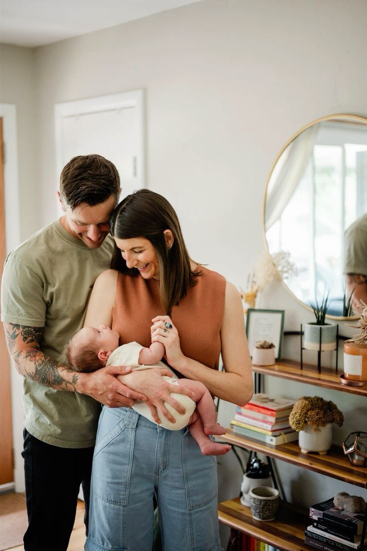 A couple shares an intimate moment with their newborn baby in a cozy home setting with natural light and modern decor.