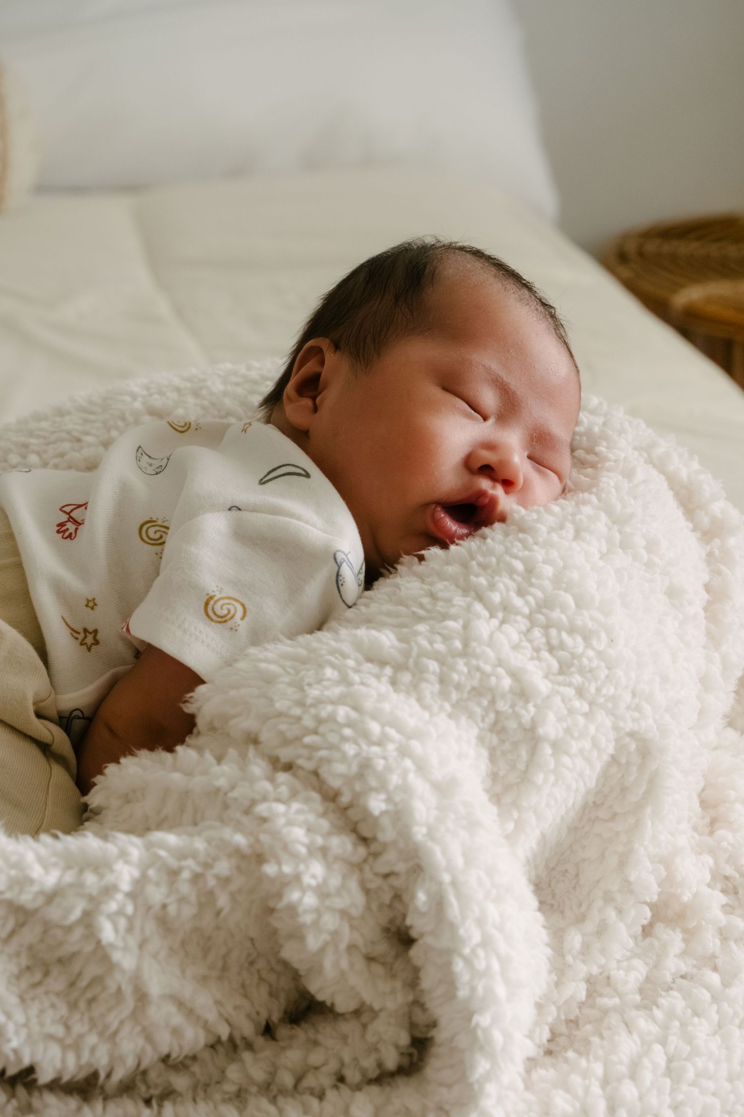 Newborn sleeping peacefully under cozy white textured blanket.