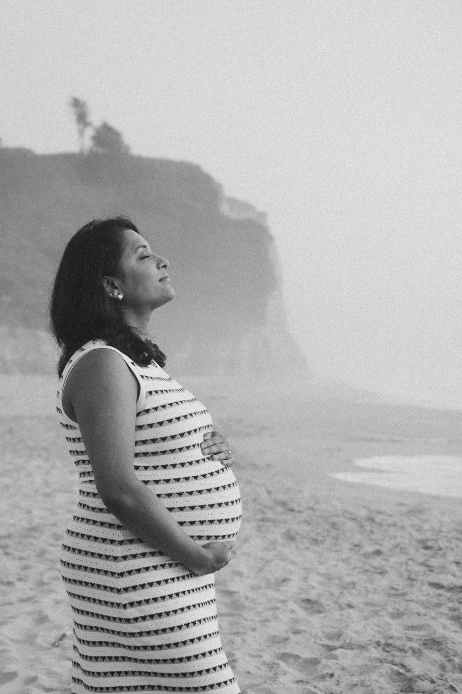 Person in striped dress stands on foggy beach with cliffs in background.