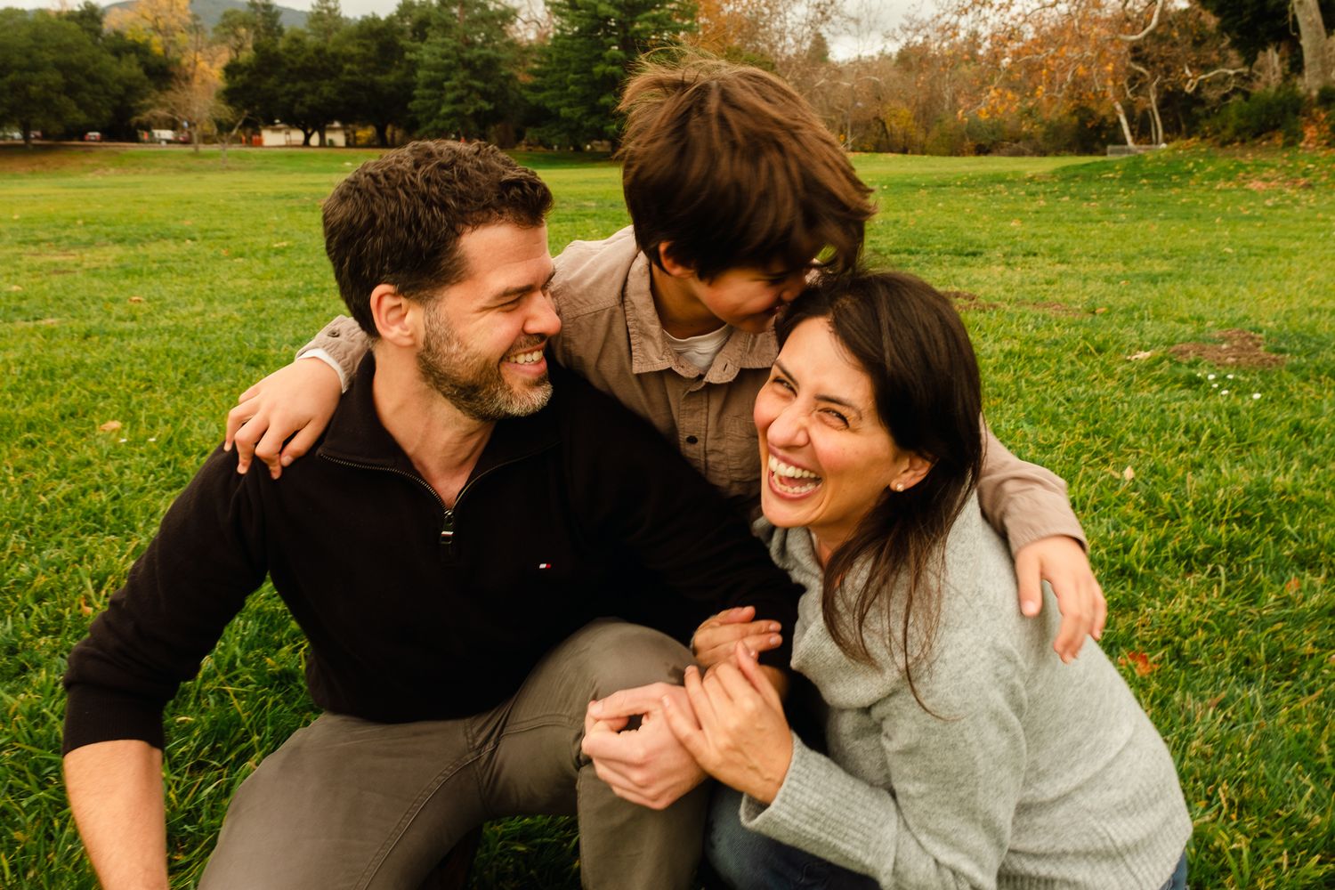 Couple sharing laughter and embraces on a grassy field during sunset.