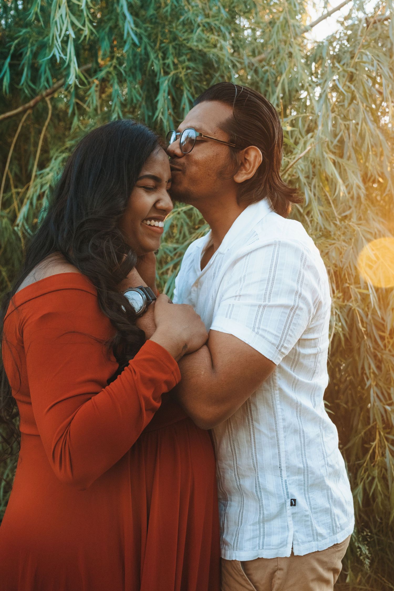 Loving couple shares tender moments against a backdrop of willow trees at sunset.