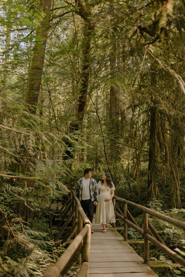 A wooden boardwalk winds through a lush green forest with tall trees and dense foliage.