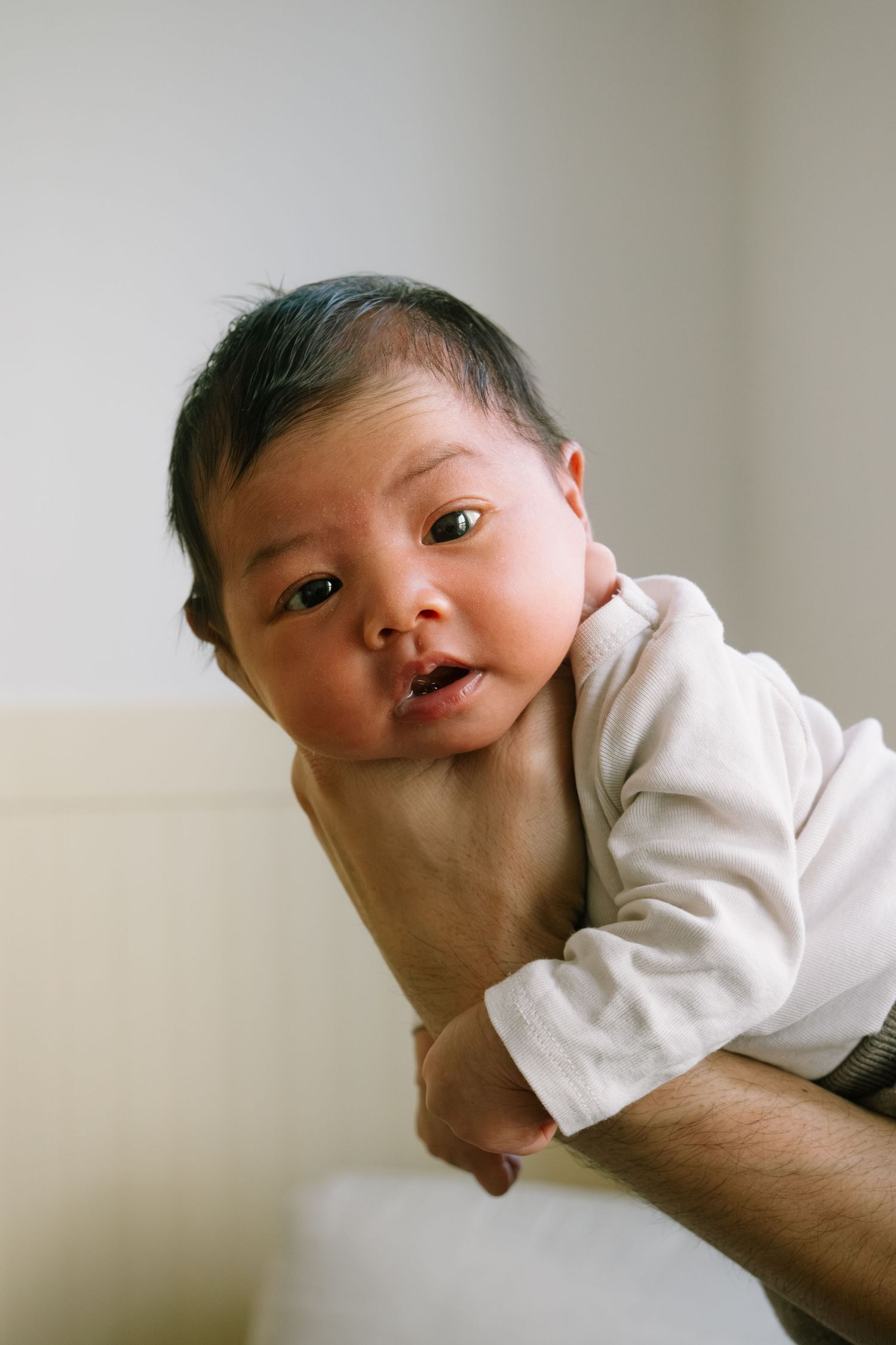Baby lying on back wearing white clothing against a light background.