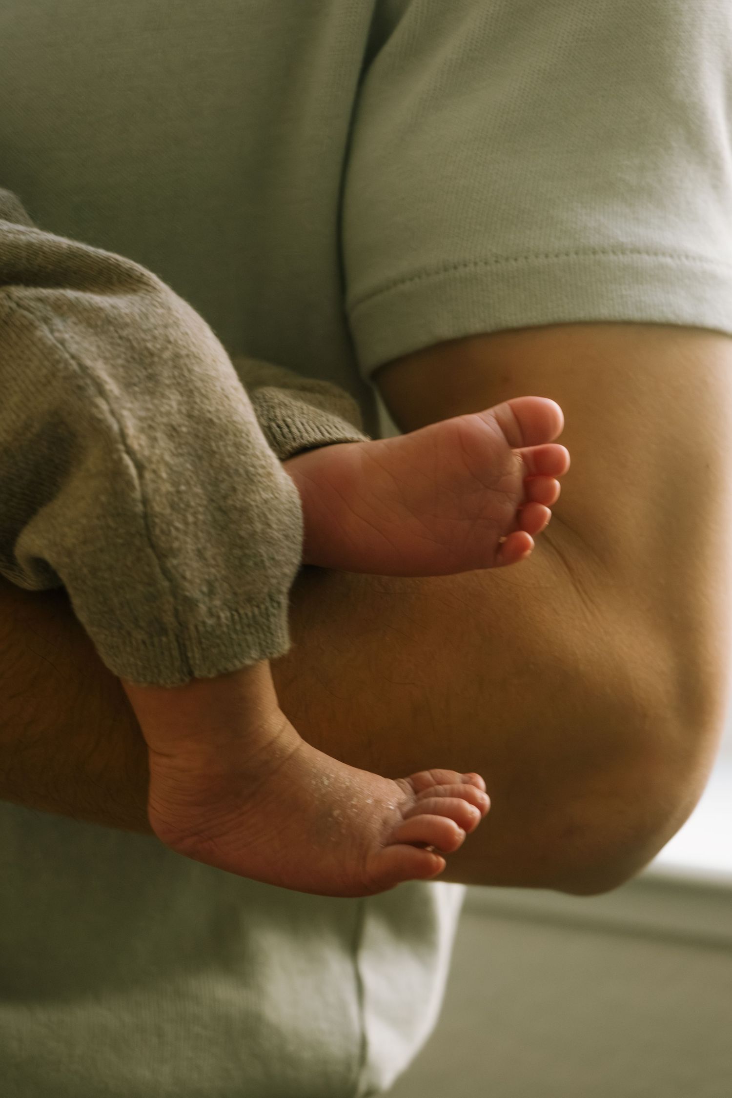 Close-up of tiny newborn baby feet resting on an adult's arm while being cradled gently.