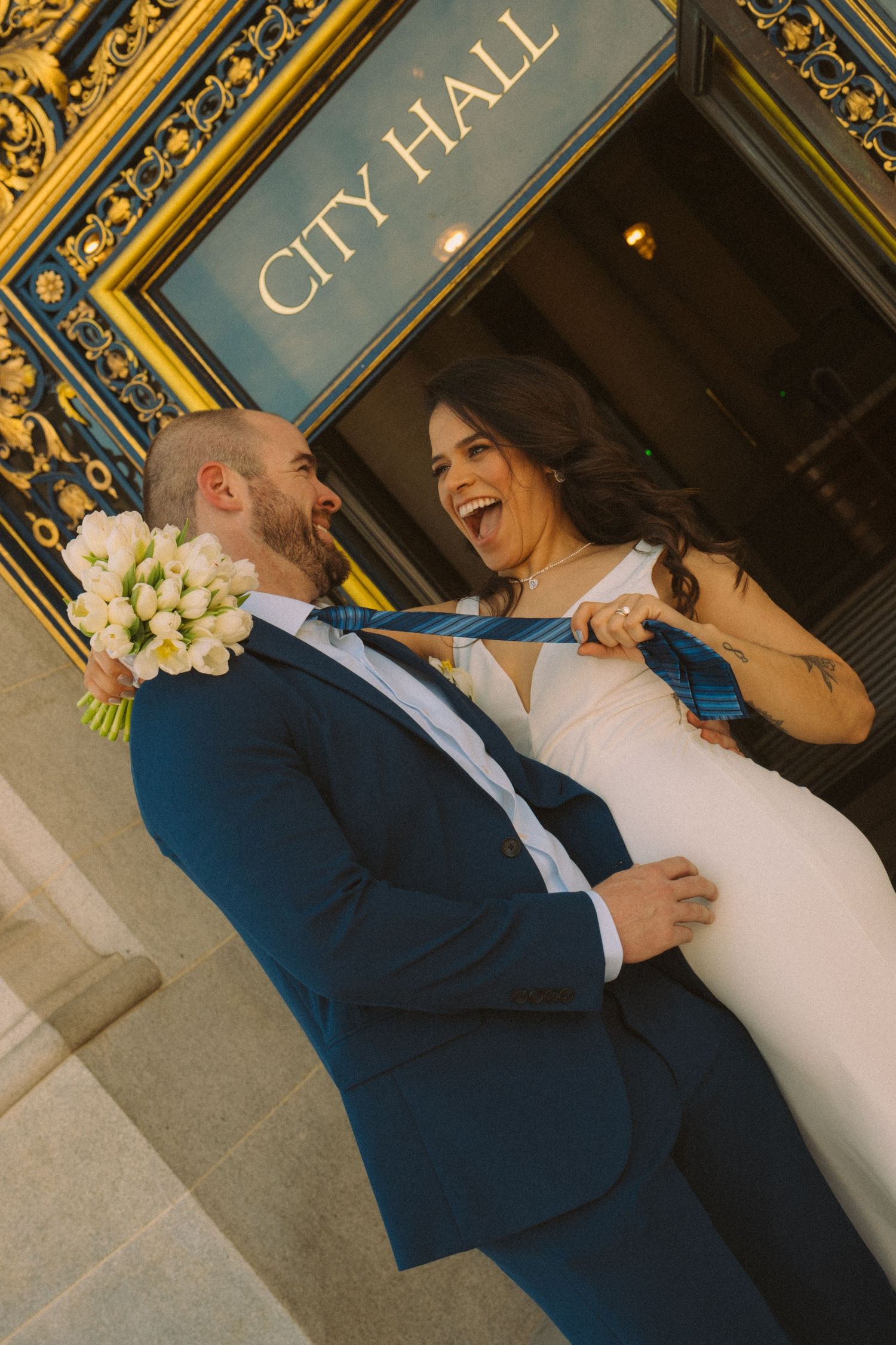 Wedding couple shares intimate moments and laughter against an ornate gold-trimmed wall with vintage lettering.