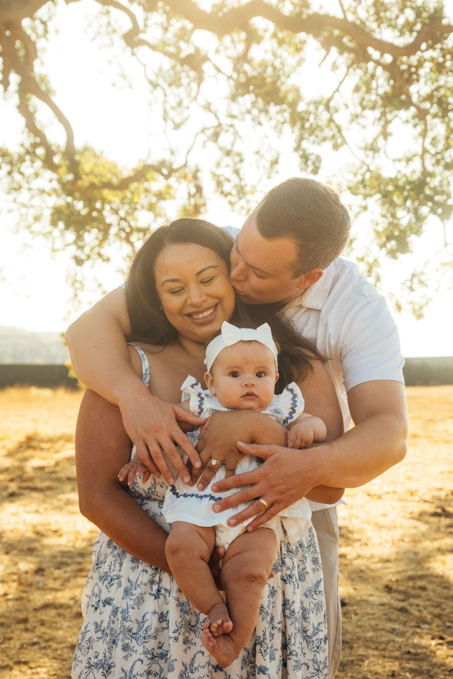 Family shares joyful moments with their baby under a tree at sunset.