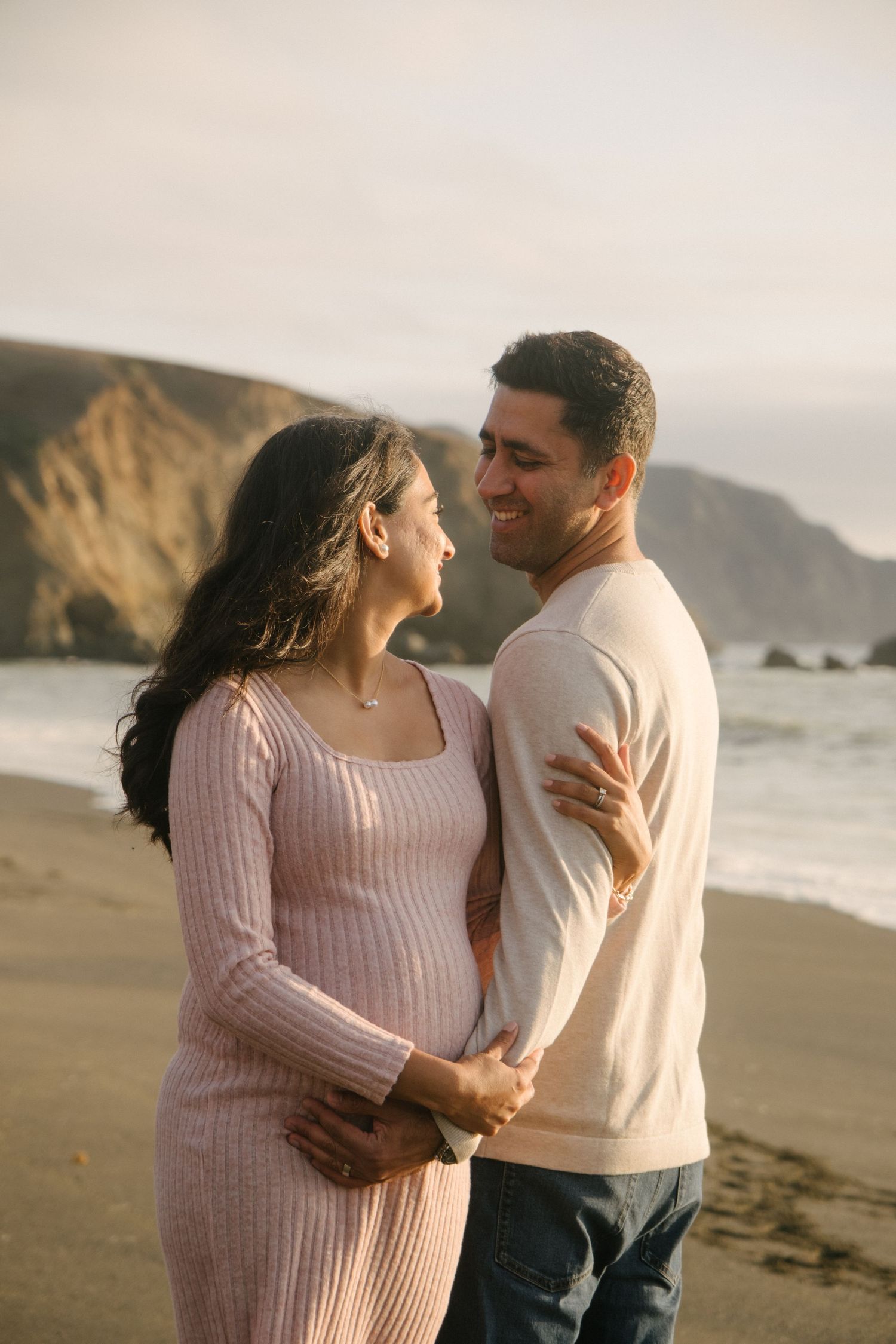 A couple shares romantic moments on a beach with dramatic coastal cliffs in the background.