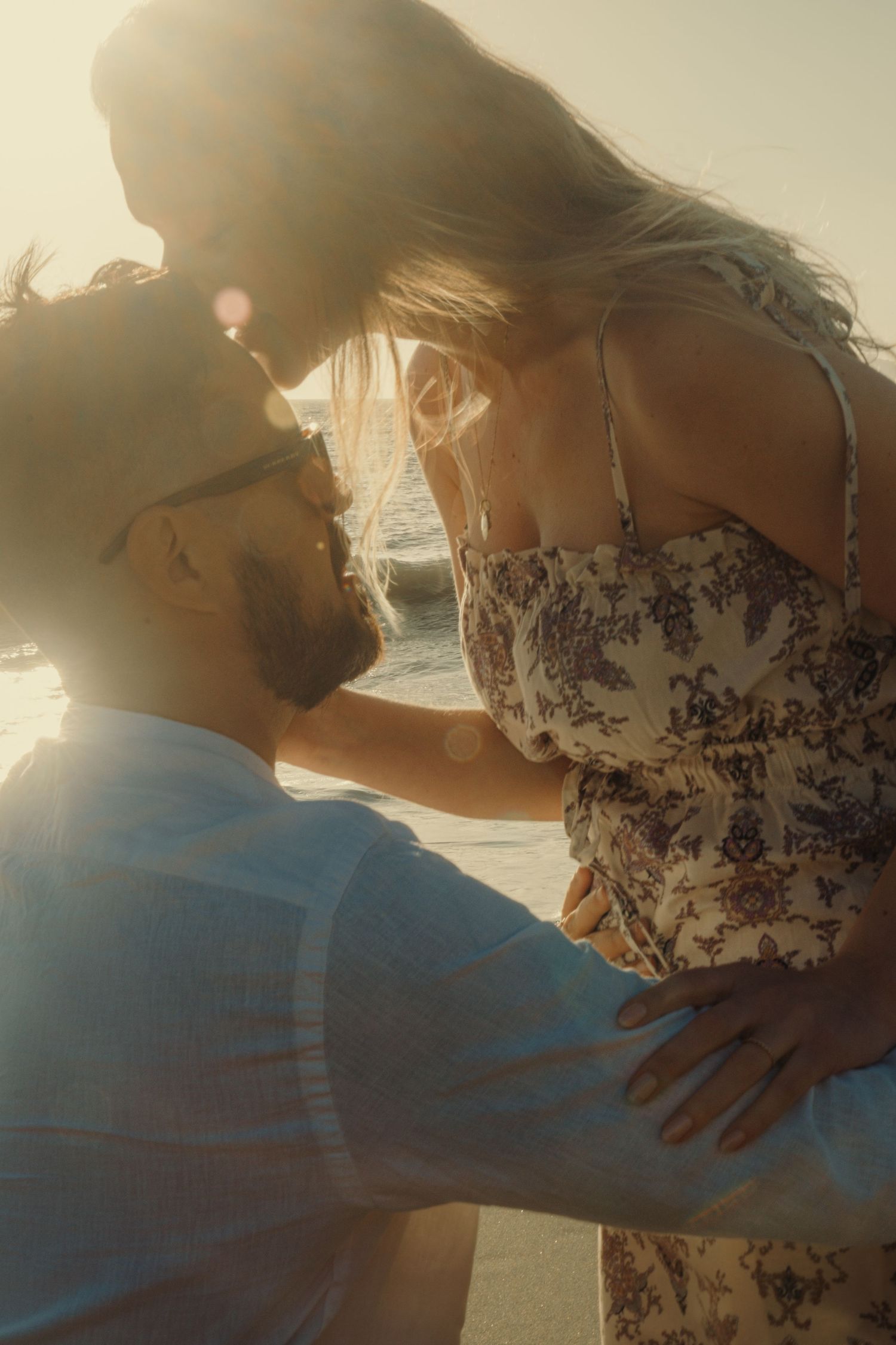 Romantic beach photoshoot at sunset with couple in casual attire.