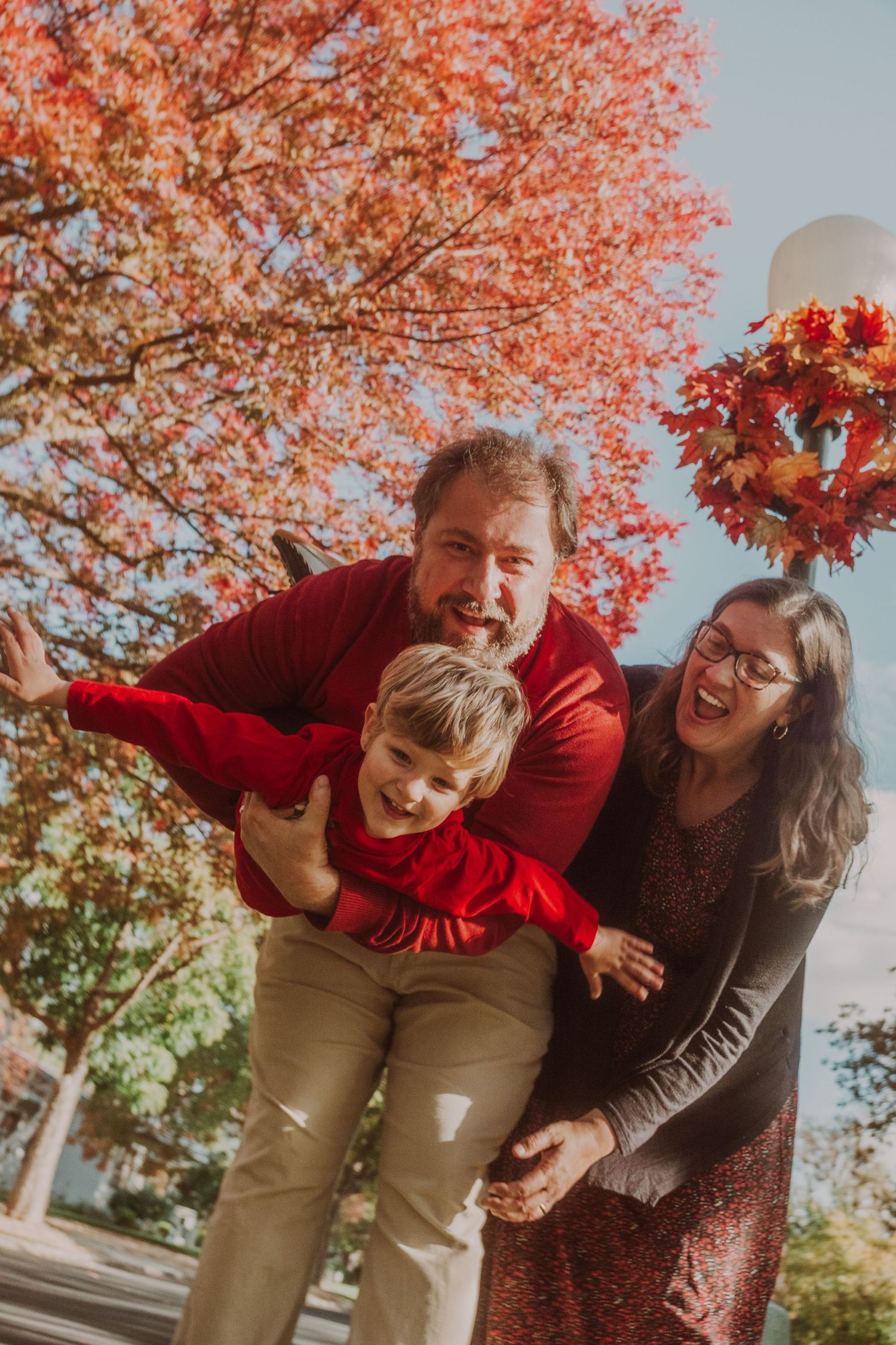 Playful family moment under vibrant orange fall trees with joyful expressions.