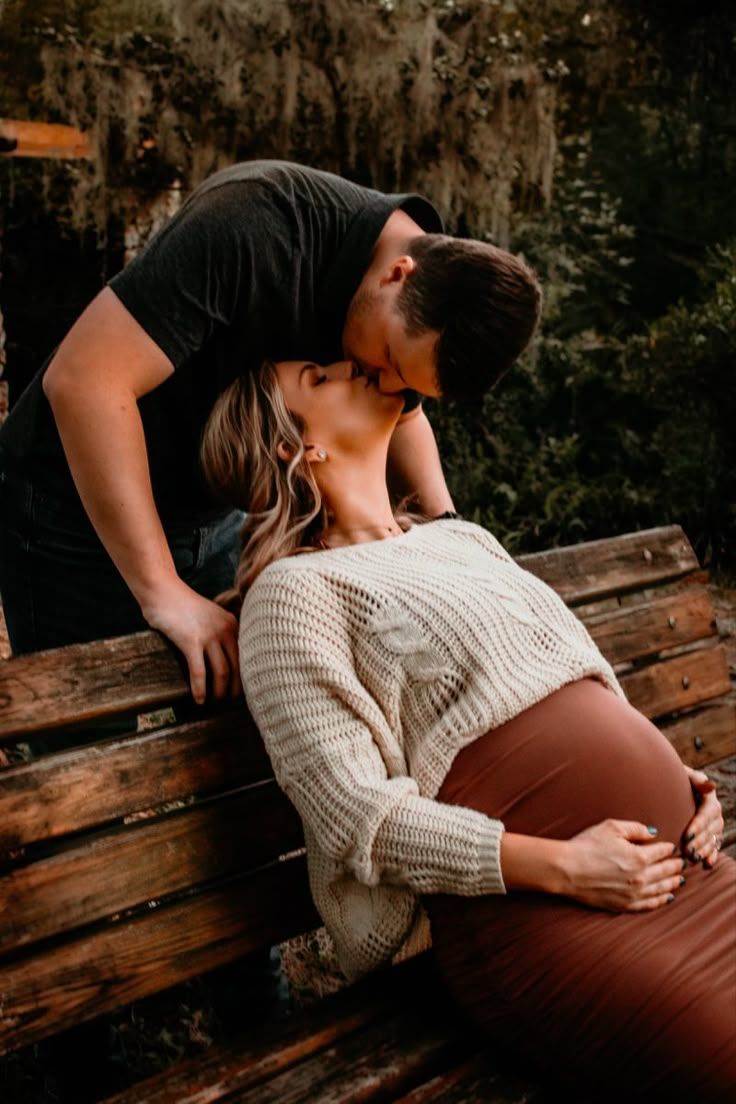Intimate maternity moment captured on a wooden bench in warm, moody lighting.