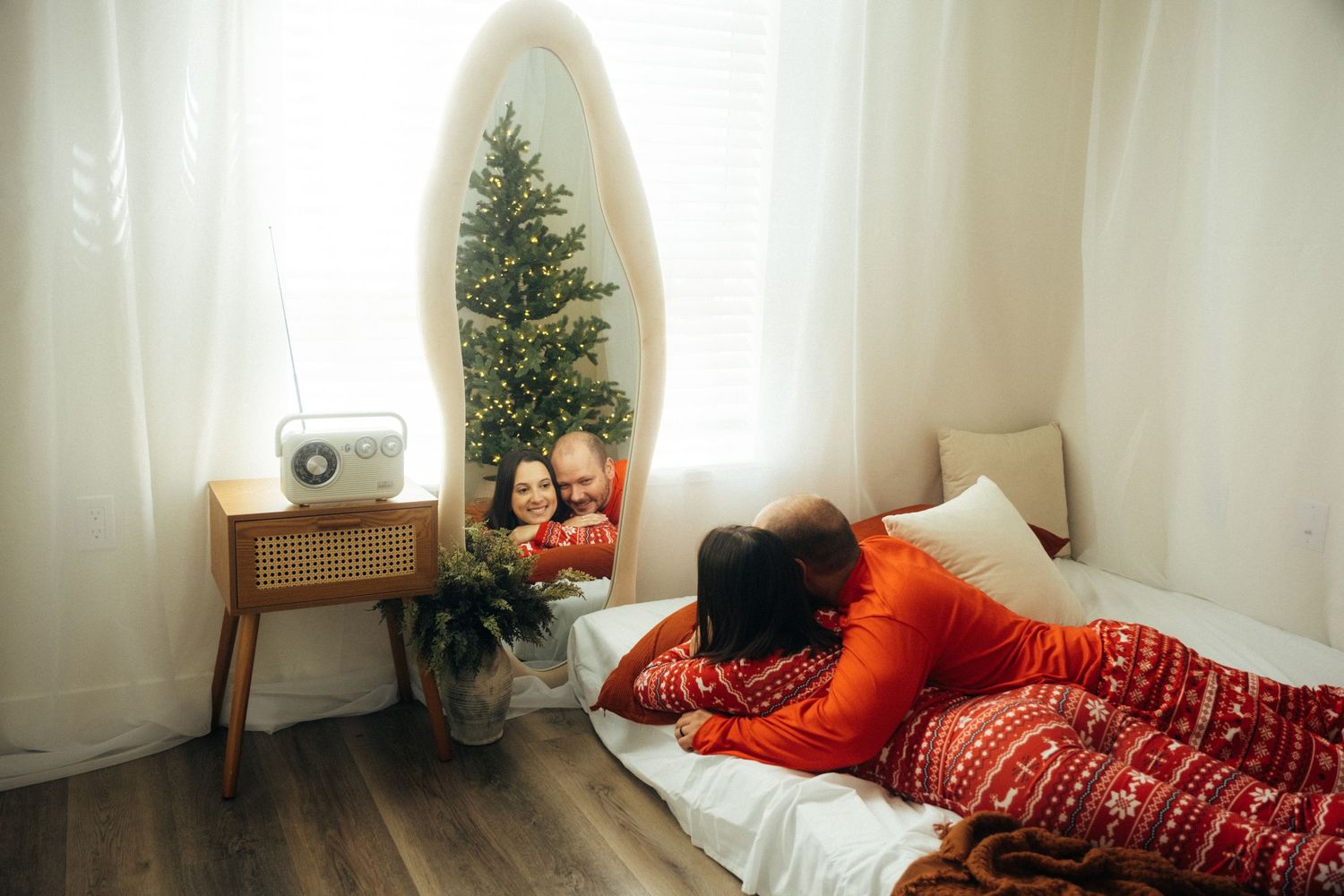 Festive holiday scene with white oval mirror, side table, and Christmas tree in a modern room setting.