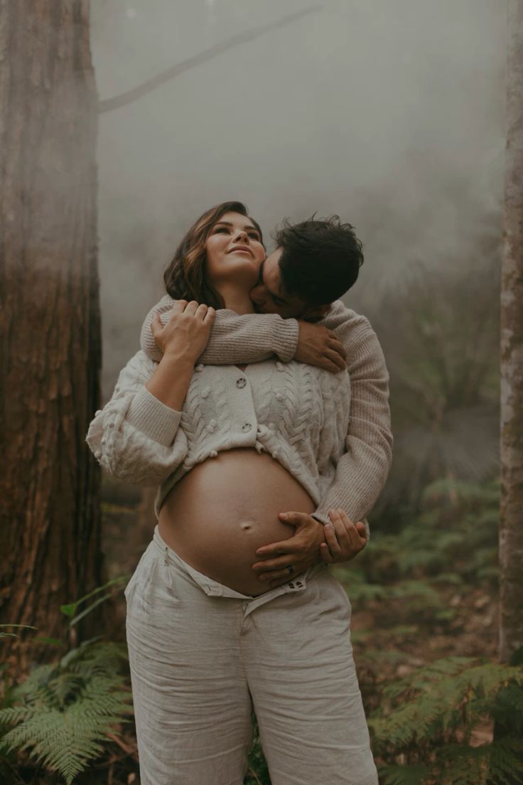 Intimate maternity photoshoot in misty forest with soft natural lighting.