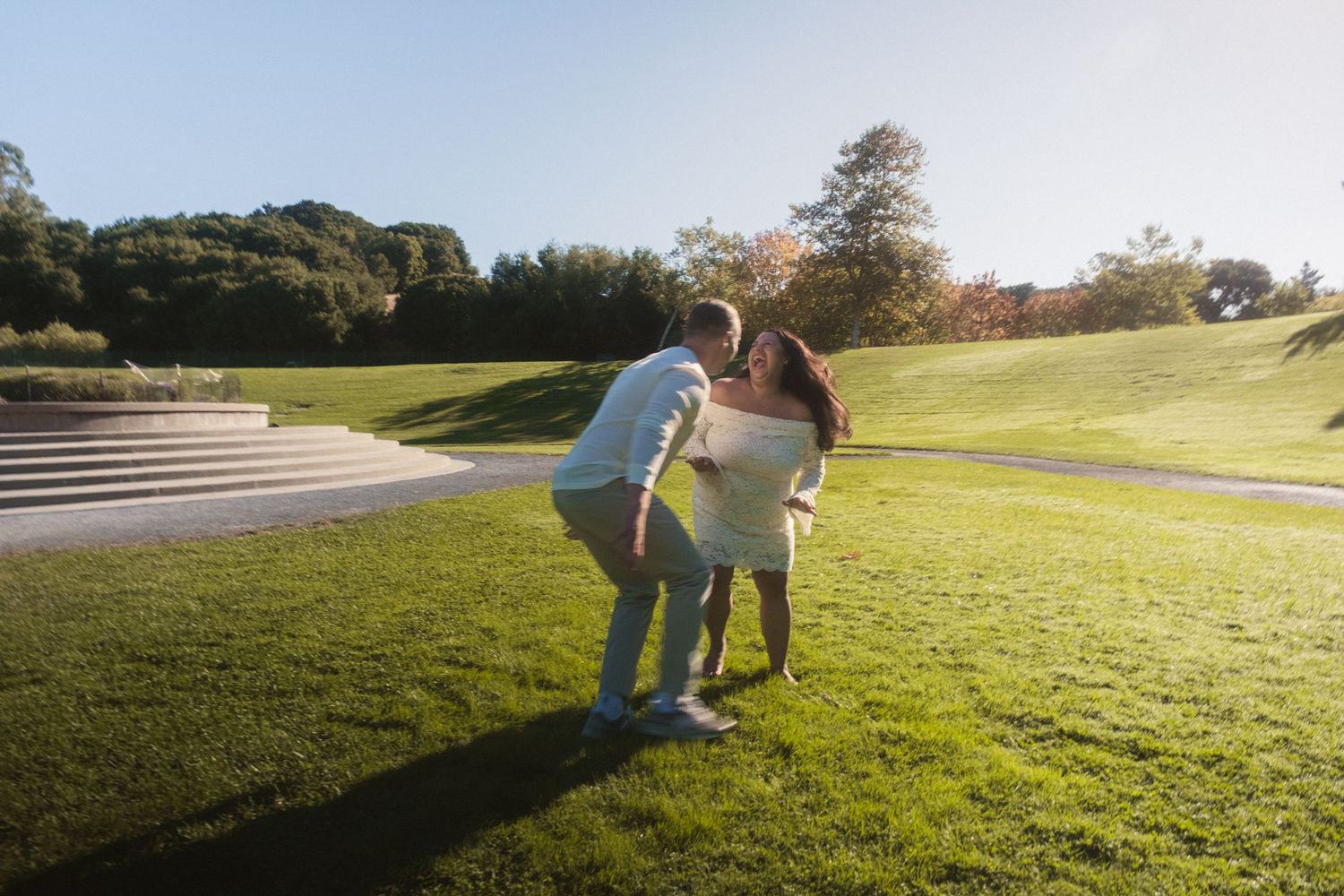 A couple runs playfully across a sunlit grassy hill.