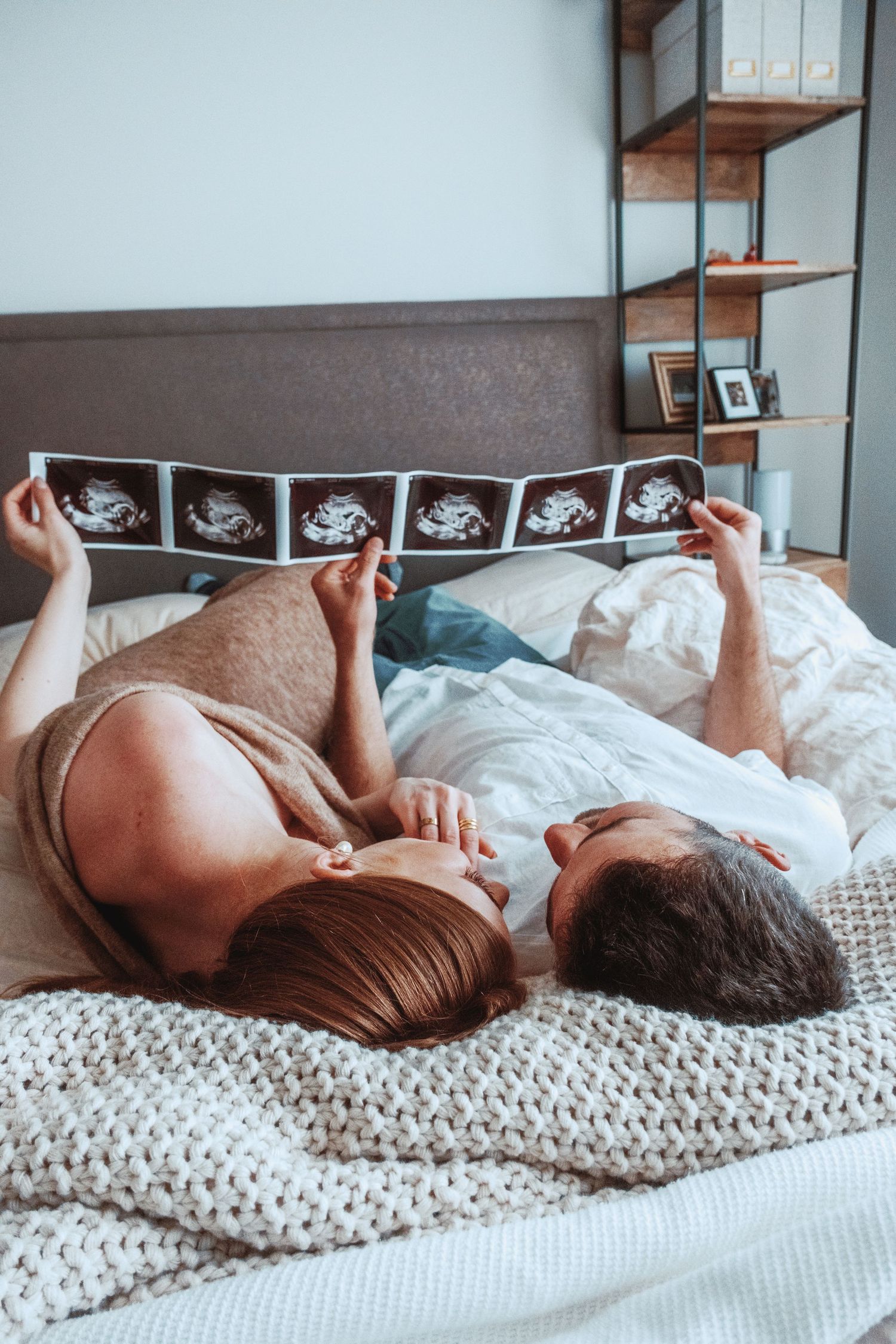 Couple lying in bed looking at ultrasound photos together.