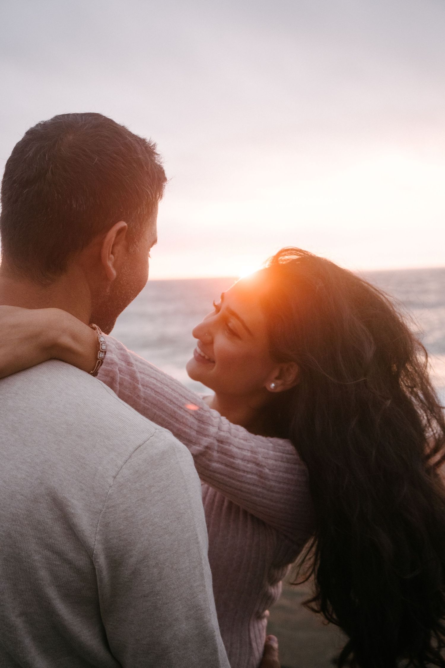 Romantic couple sharing an intimate moment at sunset on the beach with golden light illuminating their silhouettes.