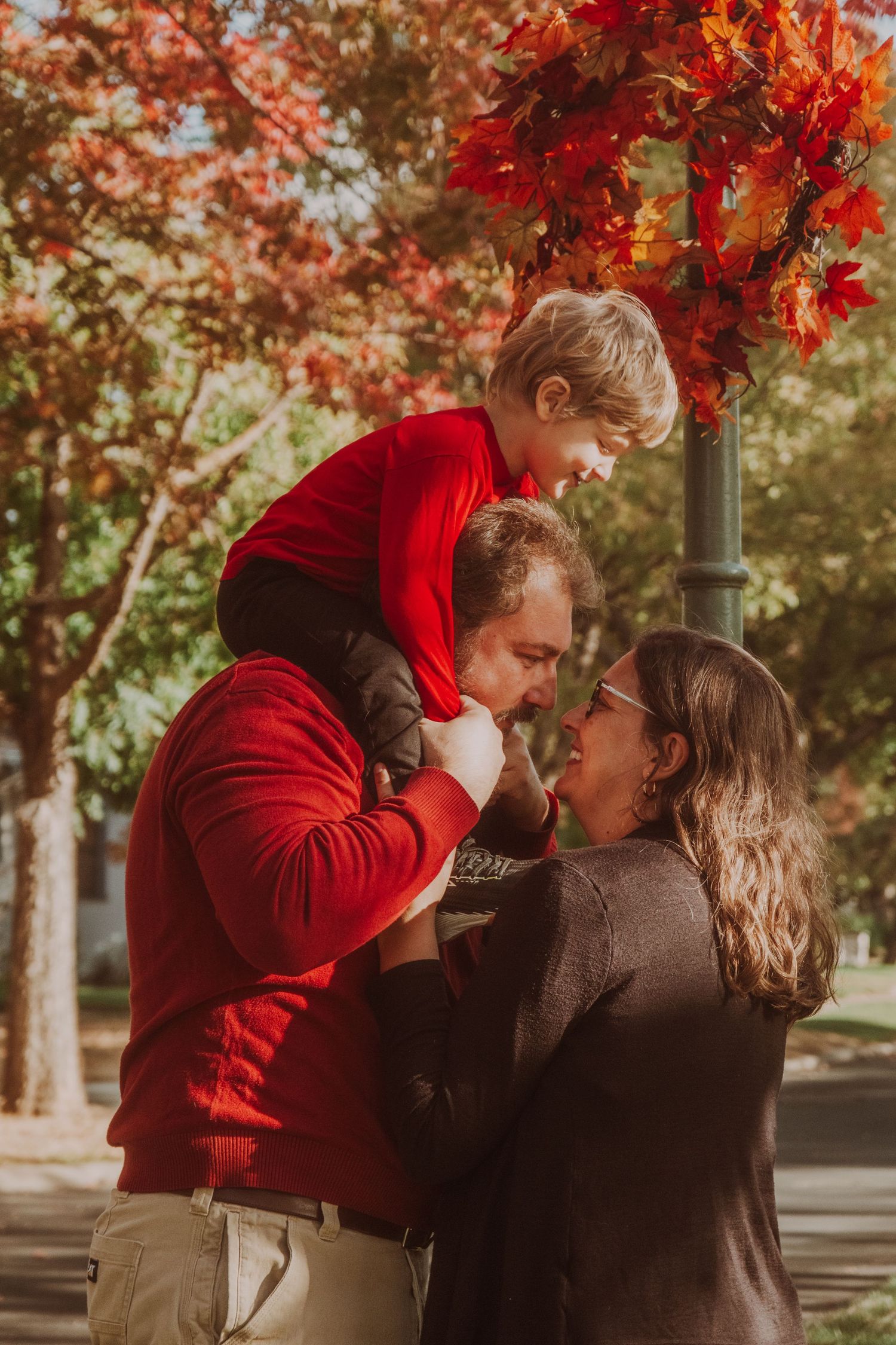 A playful family moment captured against bright red autumn foliage.