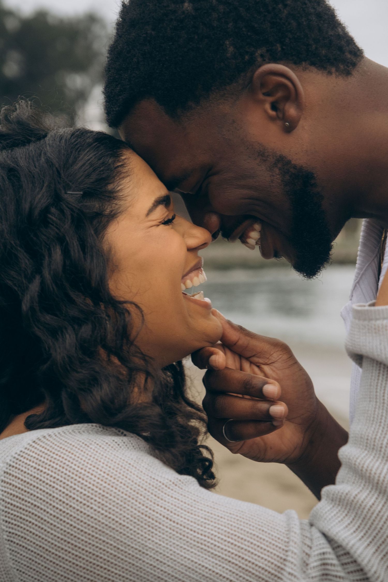A joyful couple sharing an intimate moment, touching foreheads and smiling warmly at each other outdoors.