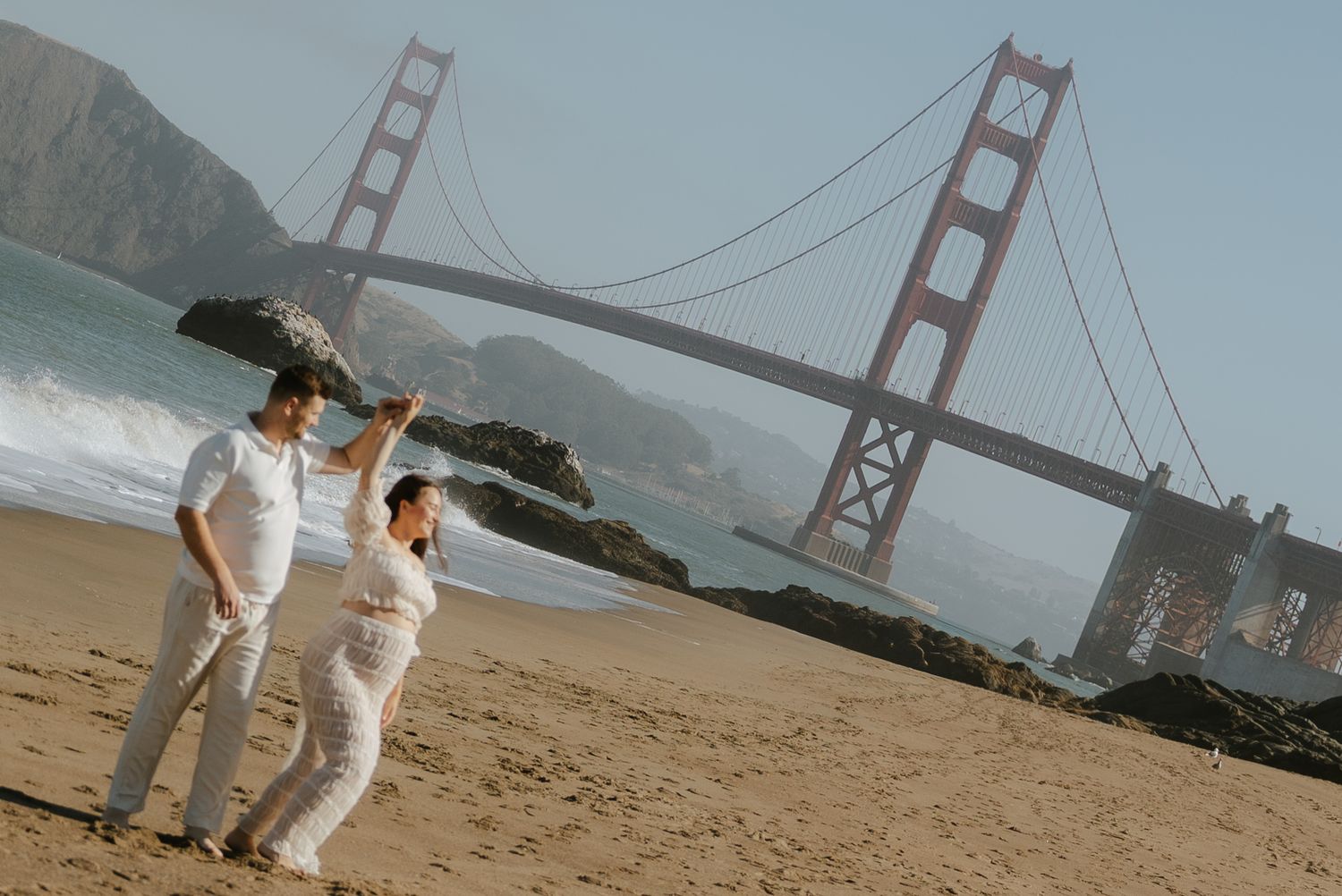 Couple poses on Baker Beach with the iconic Golden Gate Bridge backdrop in San Francisco, CA.
