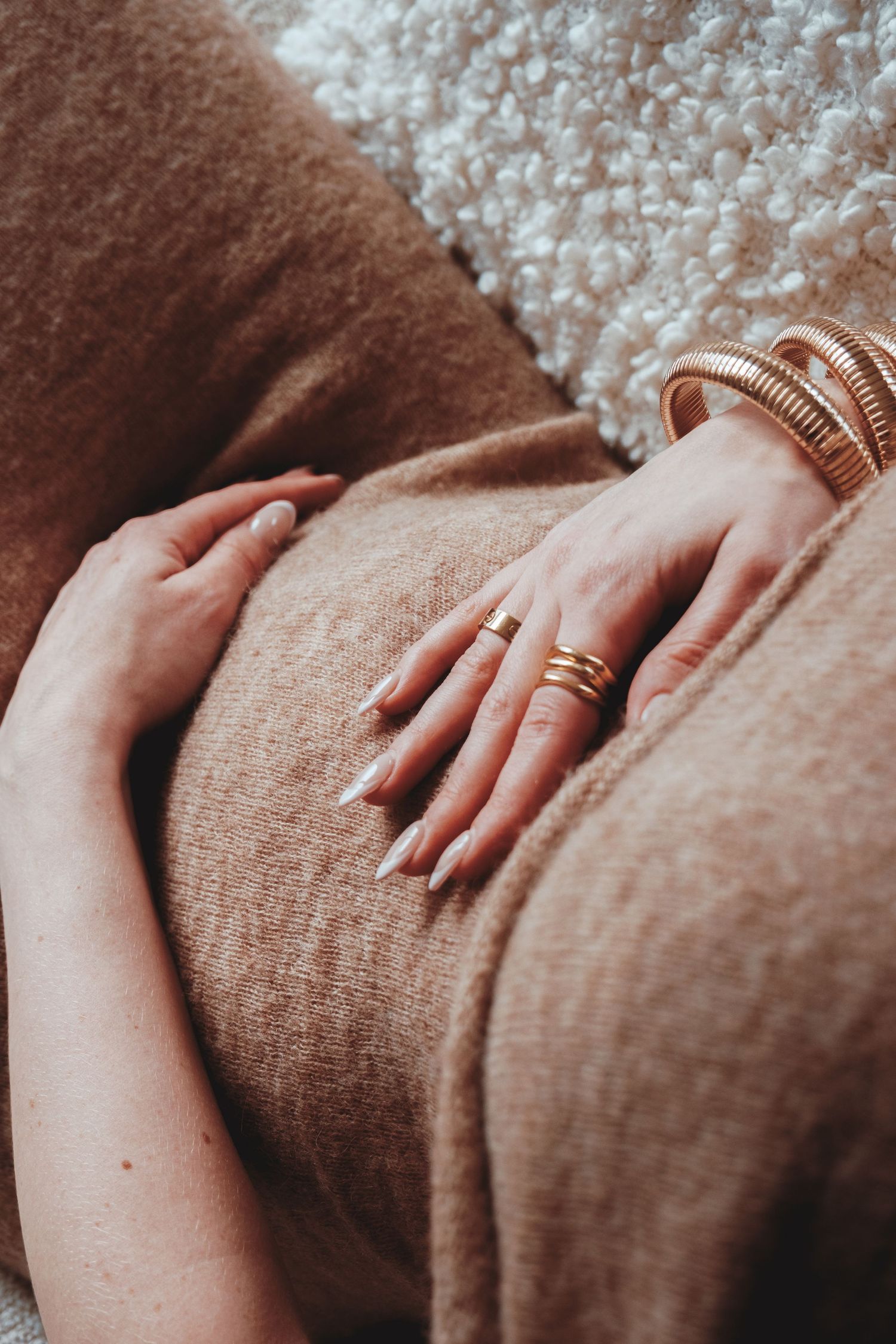 Close up of hands with wedding rings resting on brown fabric.