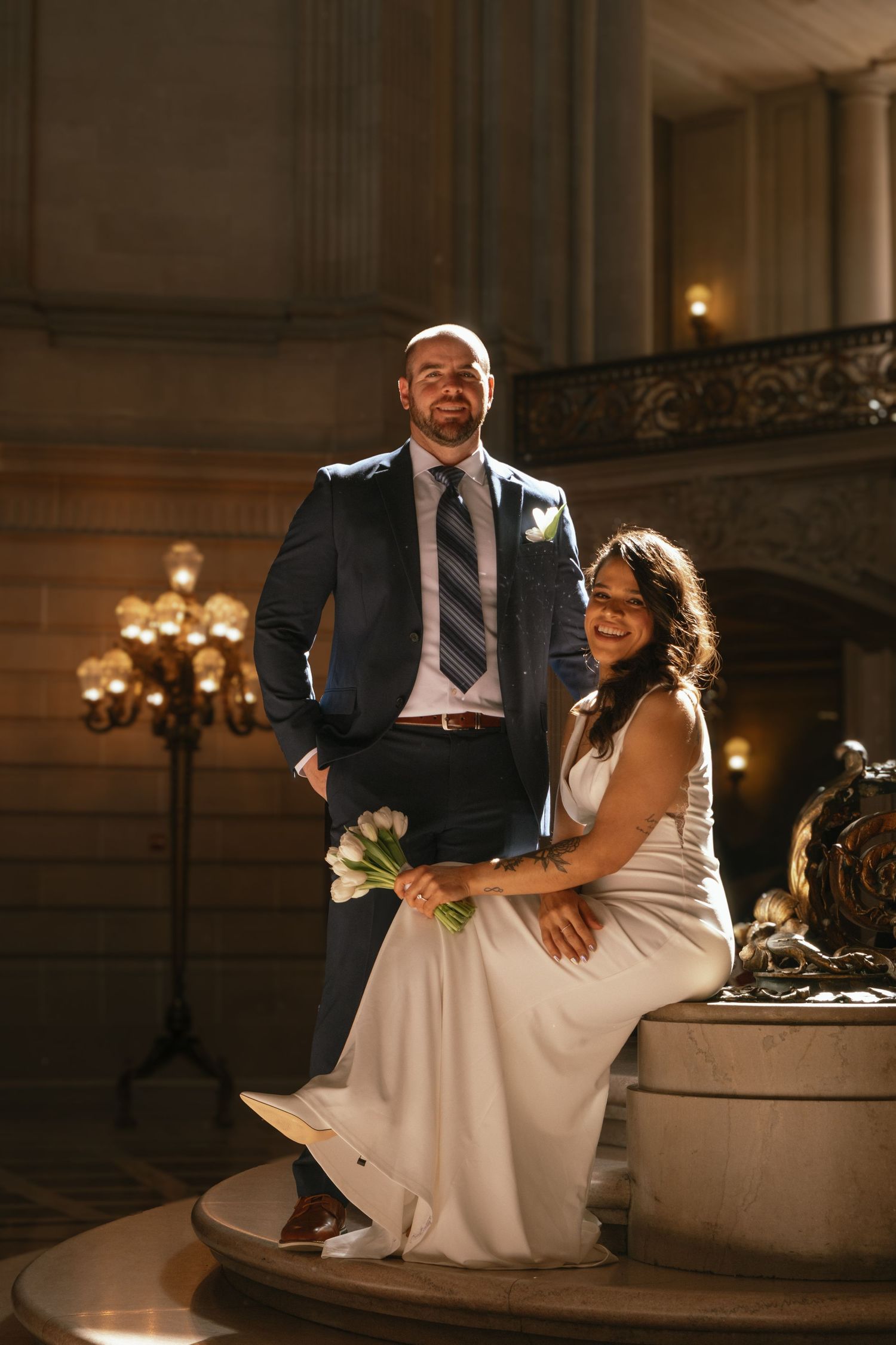 Newlyweds share an intimate moment sitting on marble steps in an elegant venue with warm lighting.