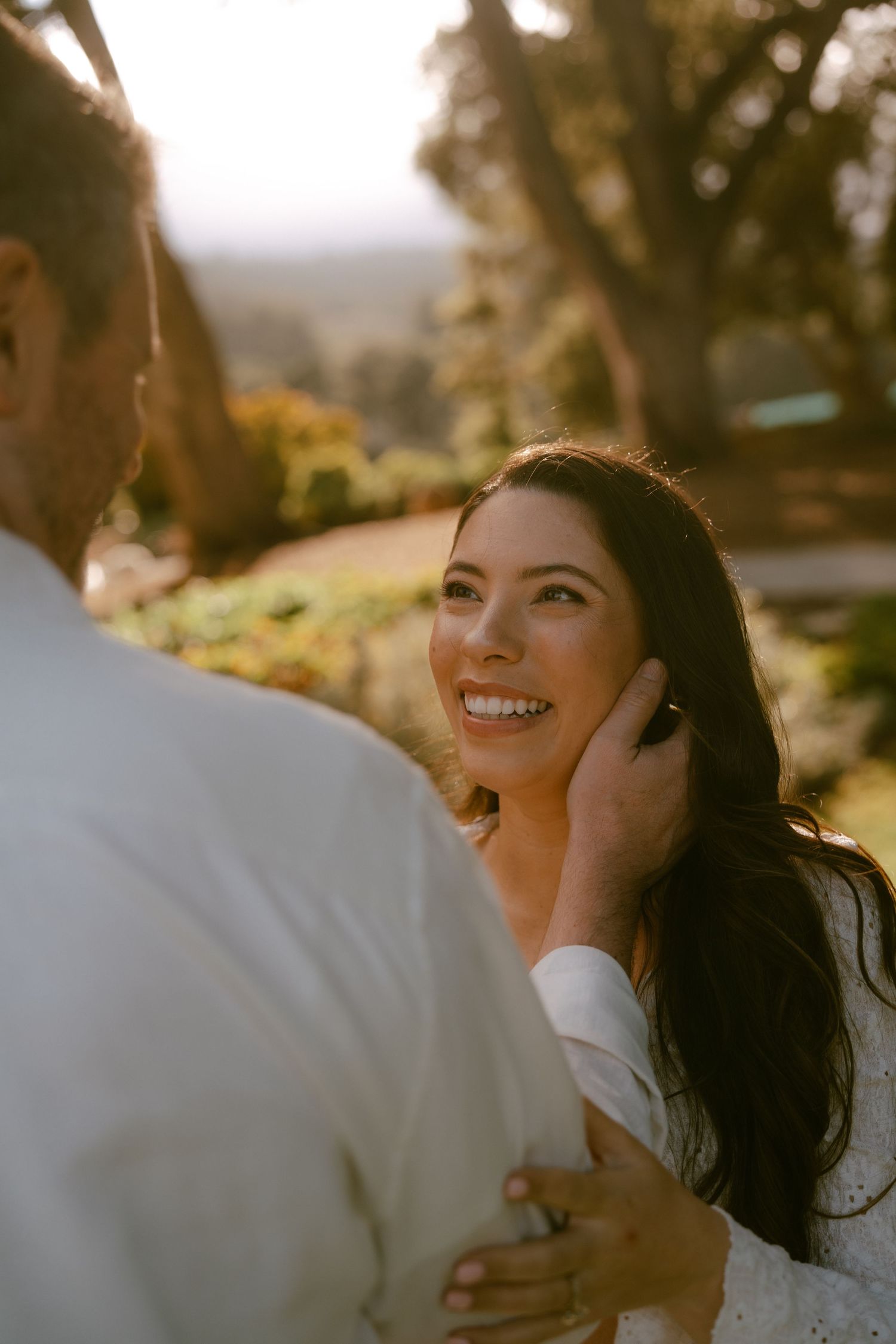 A smiling bride gazes lovingly at her partner during a golden hour outdoor wedding ceremony.