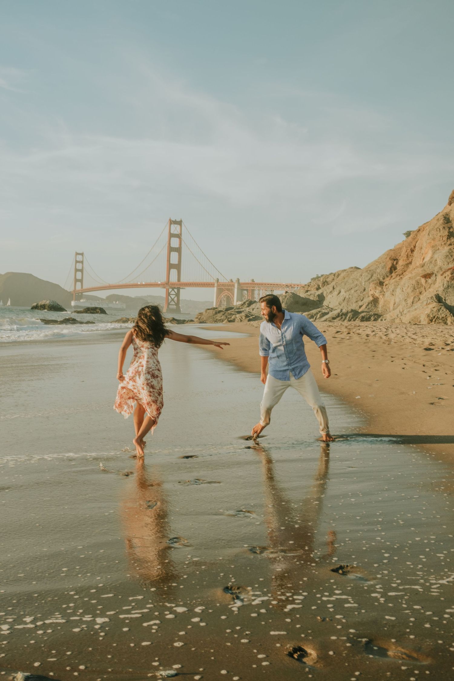 Two people playing and splashing in the waves at Baker Beach near the Golden Gate Bridge.
