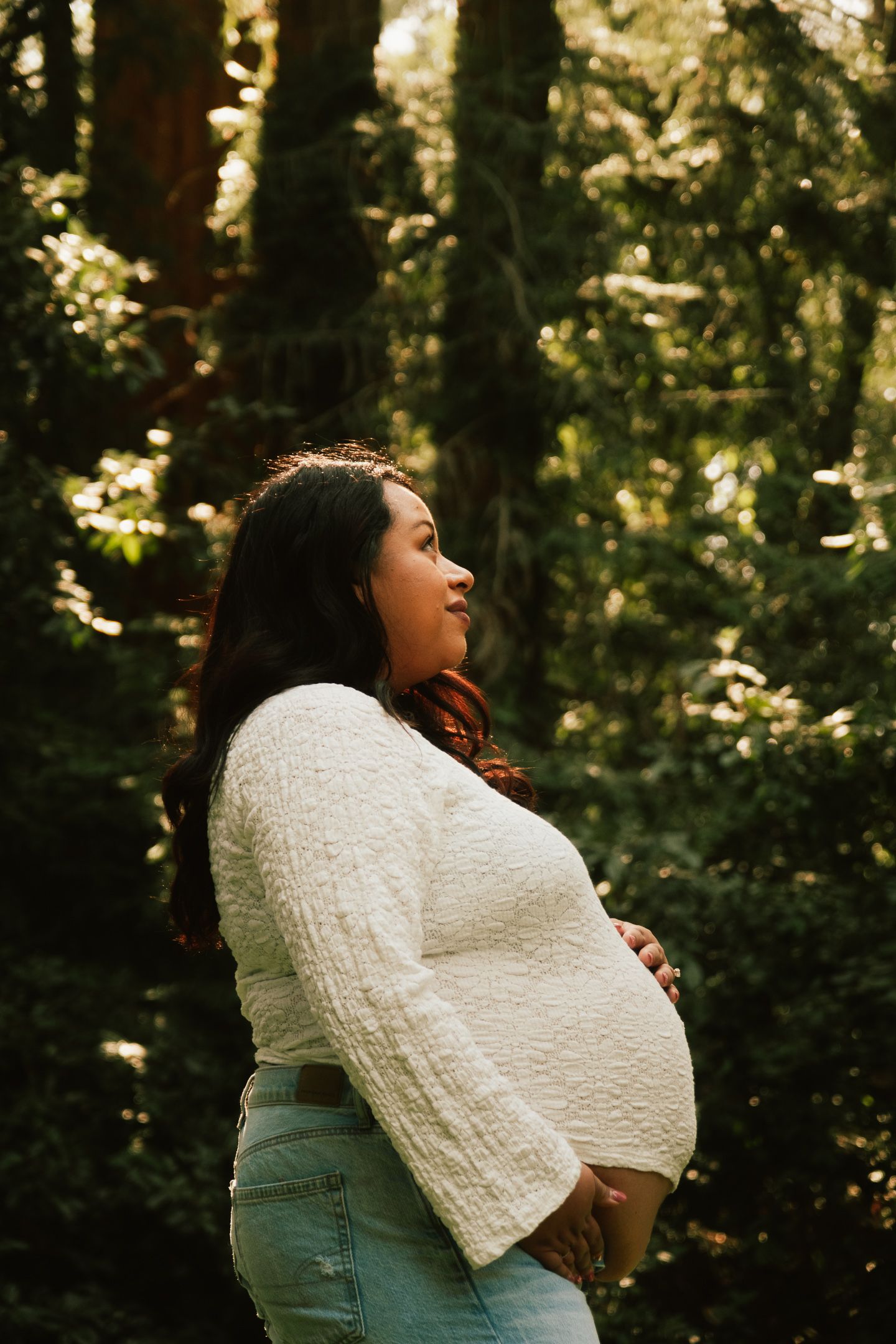 Person in white sweater laughing joyfully in a sunlit forest setting.
