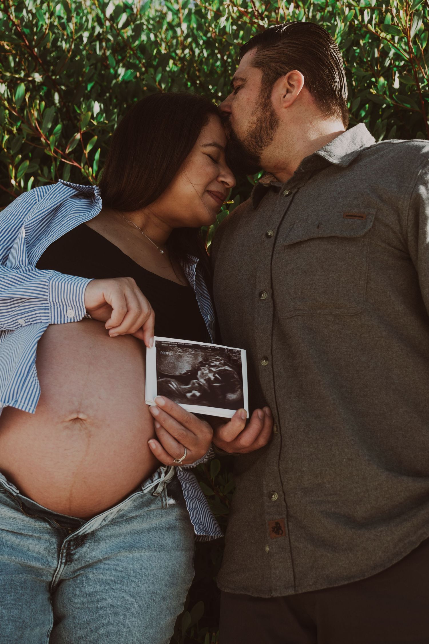 An expectant couple shares an intimate moment while holding ultrasound photos.