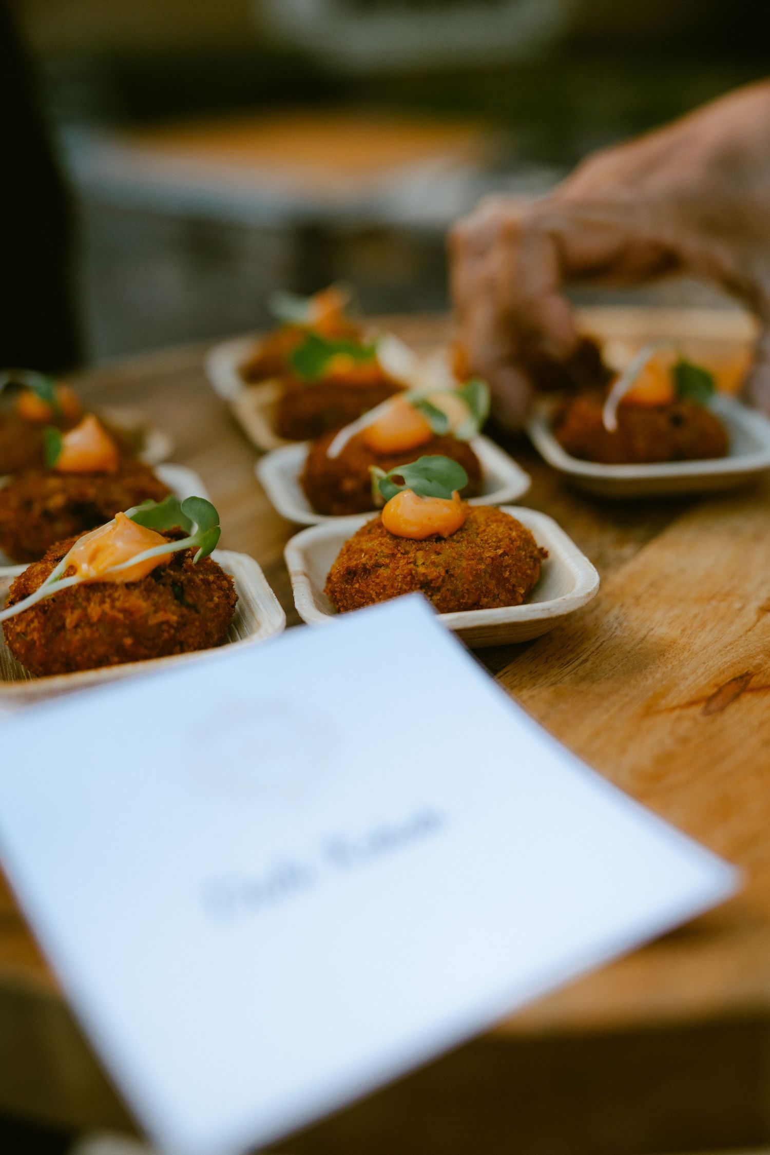 Crispy fried arancini bites topped with garnish served in small white dishes on a wooden board at a catered event.