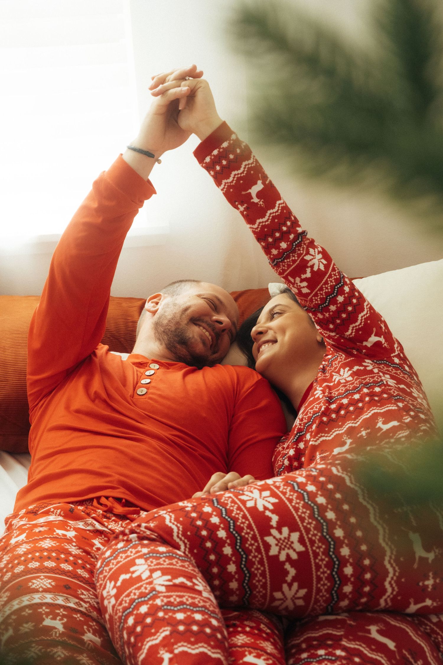A couple in matching holiday pajamas holding hands while lying down together.