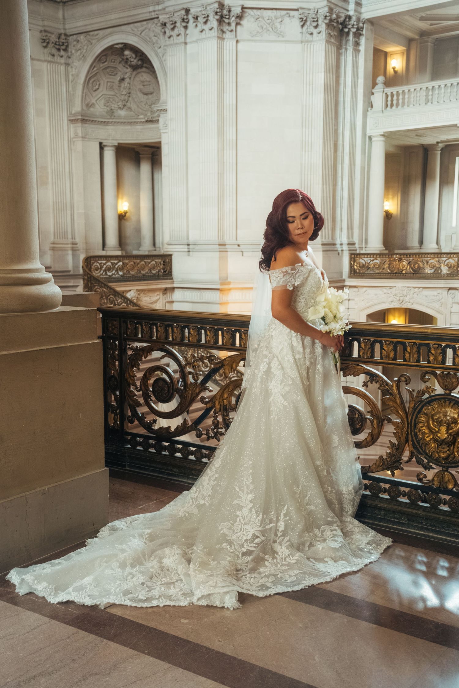 Bride in lace wedding gown with cathedral train posing by ornate railing.