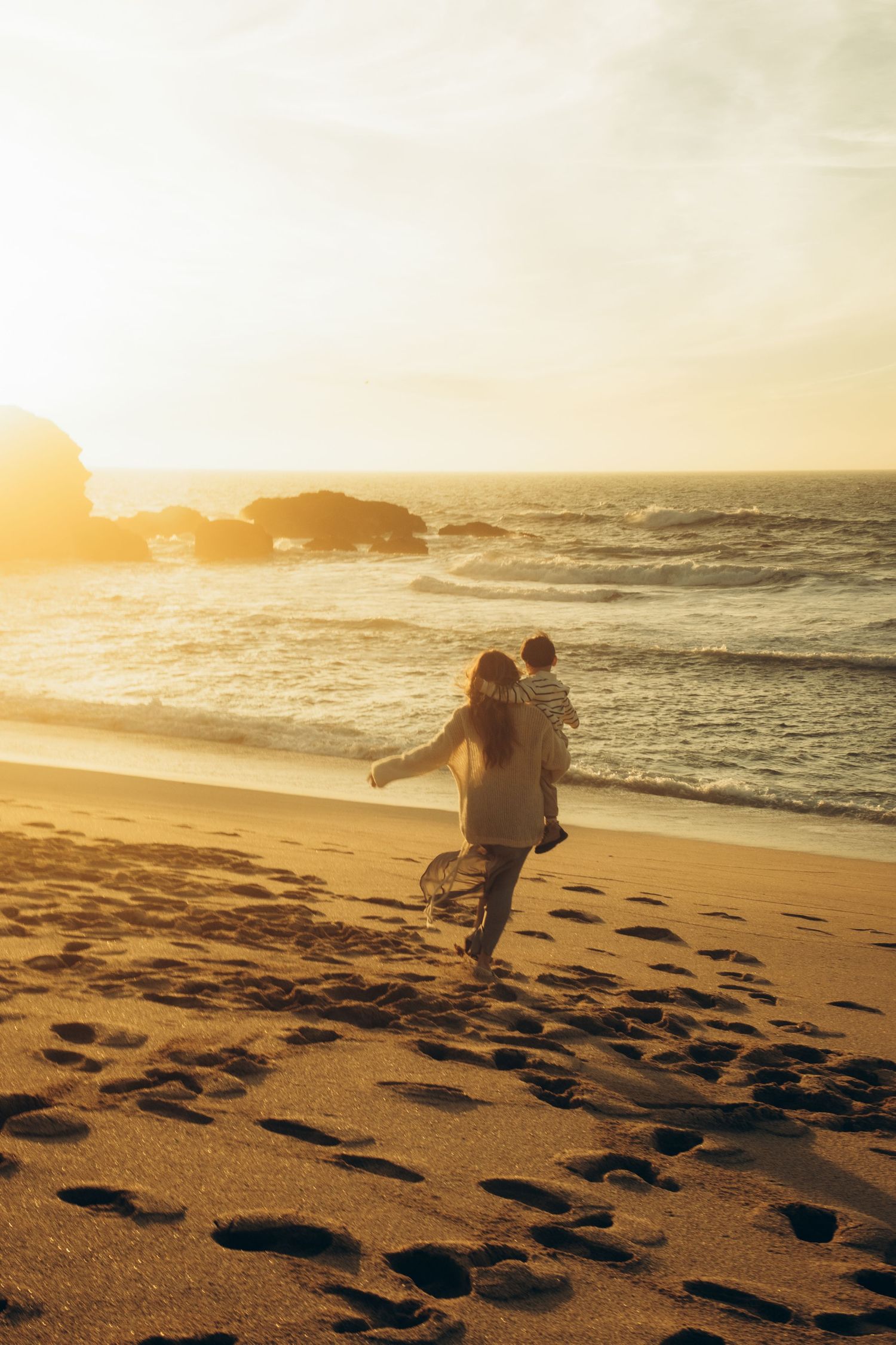 Silhouette of person running on sandy beach at sunset with ocean waves and footprints in golden light.