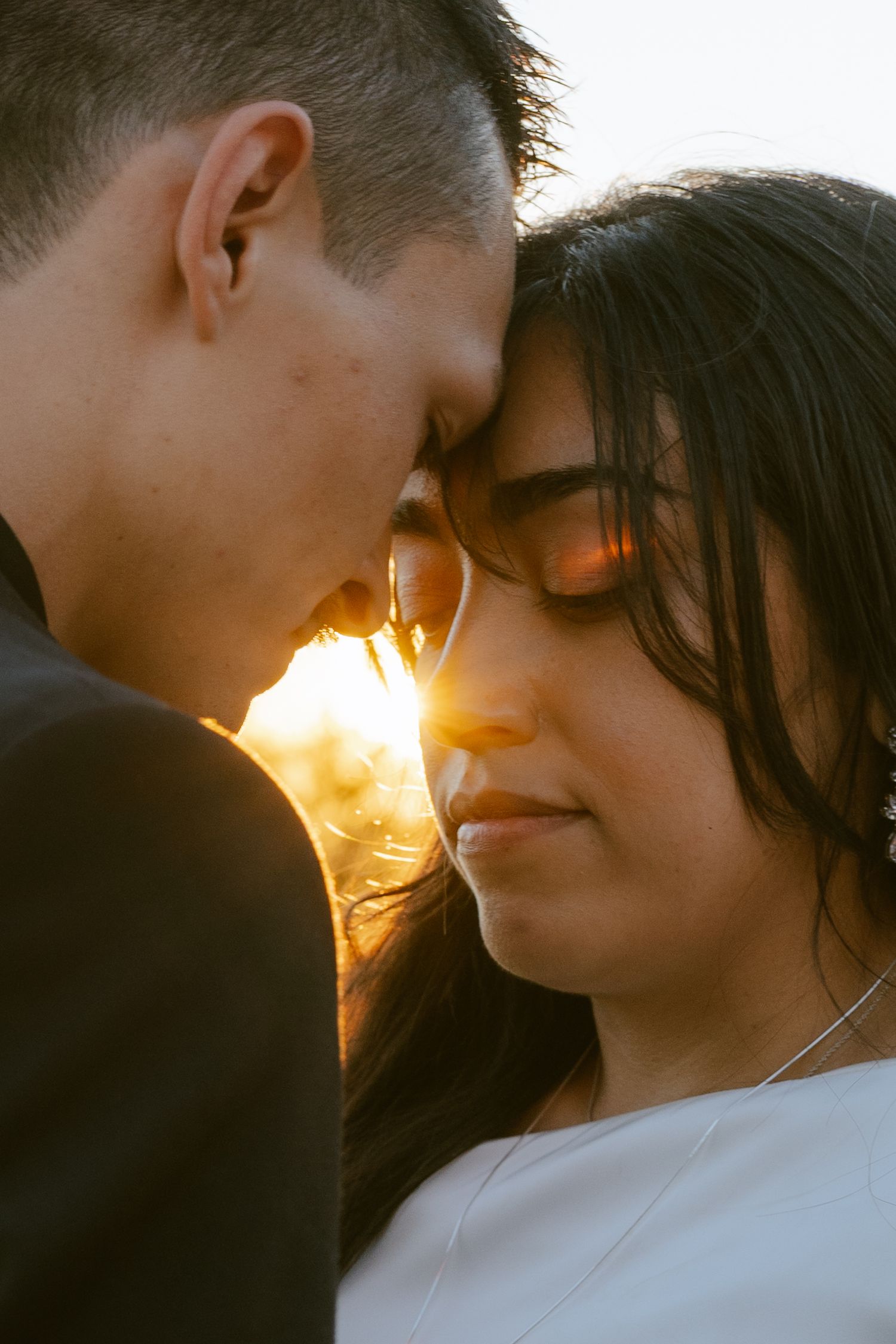 Couple sharing an intimate moment at golden hour sunset, foreheads touching romantically outdoors.