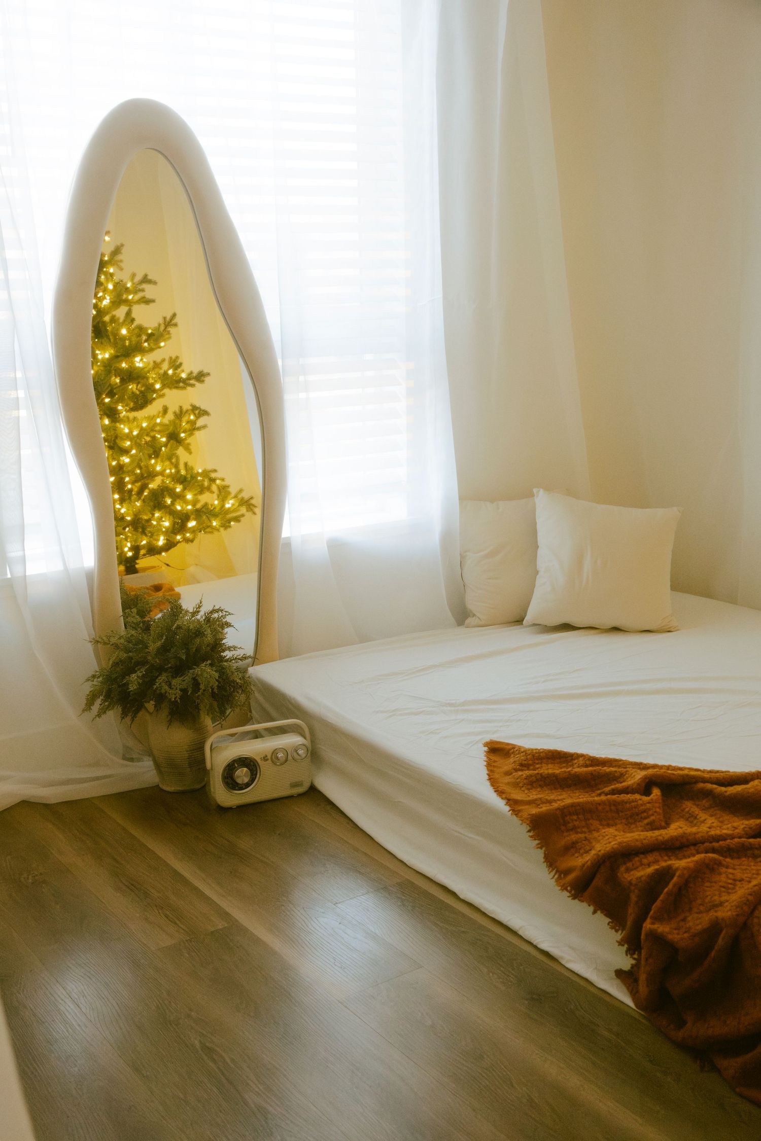 A cozy bedroom with a surfboard mirror reflecting a glowing Christmas tree and white bedding.