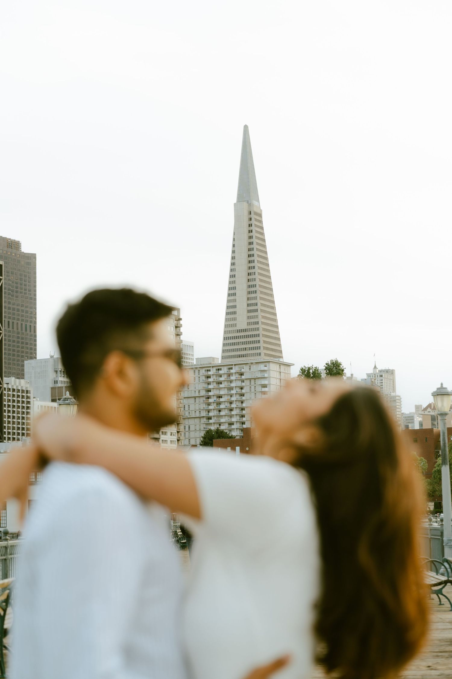 Couple embracing in front of the Transamerica Pyramid in San Francisco on a cloudy day.