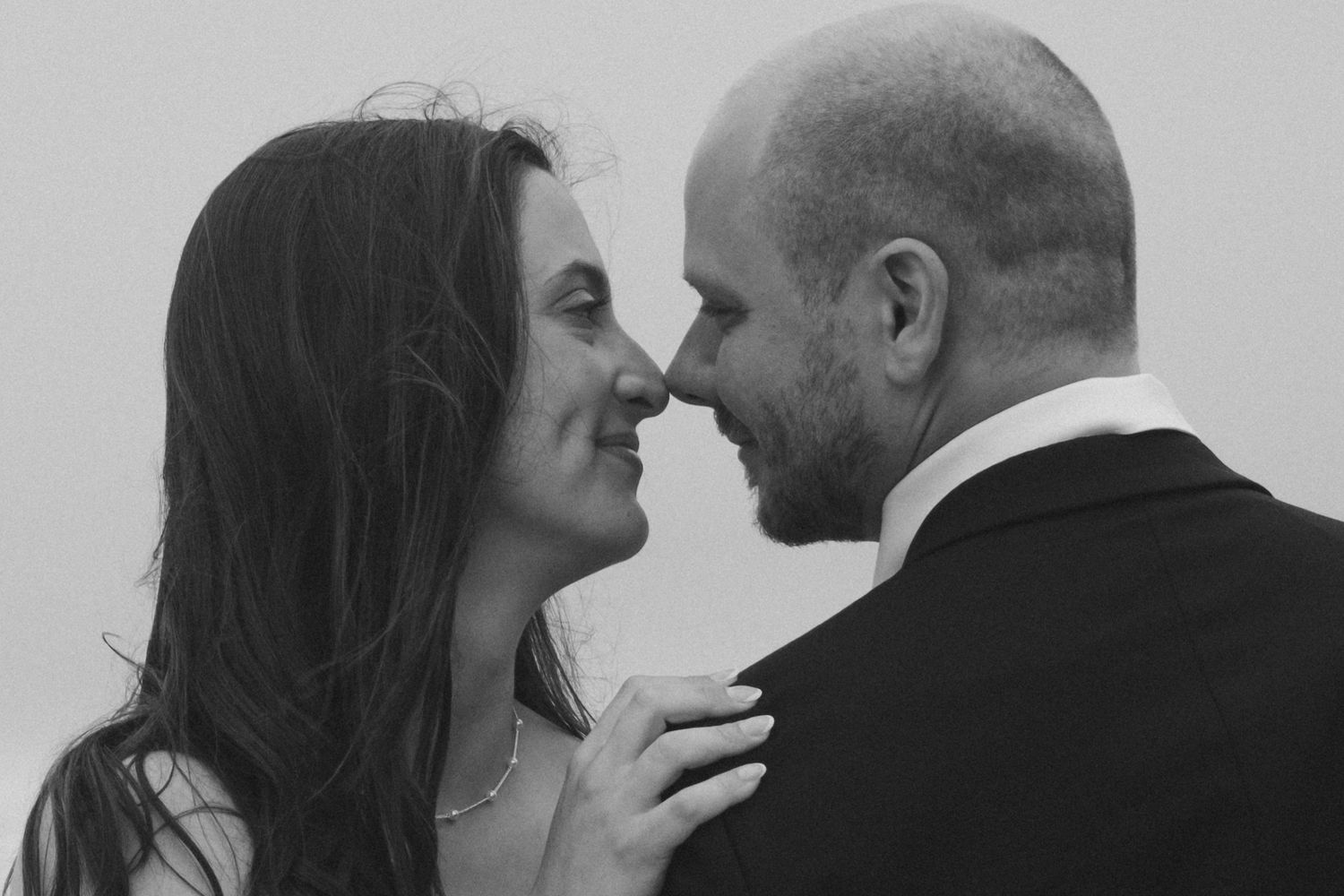 Black and white photo of a couple sharing a romantic moment, nearly kissing, dressed in wedding attire.