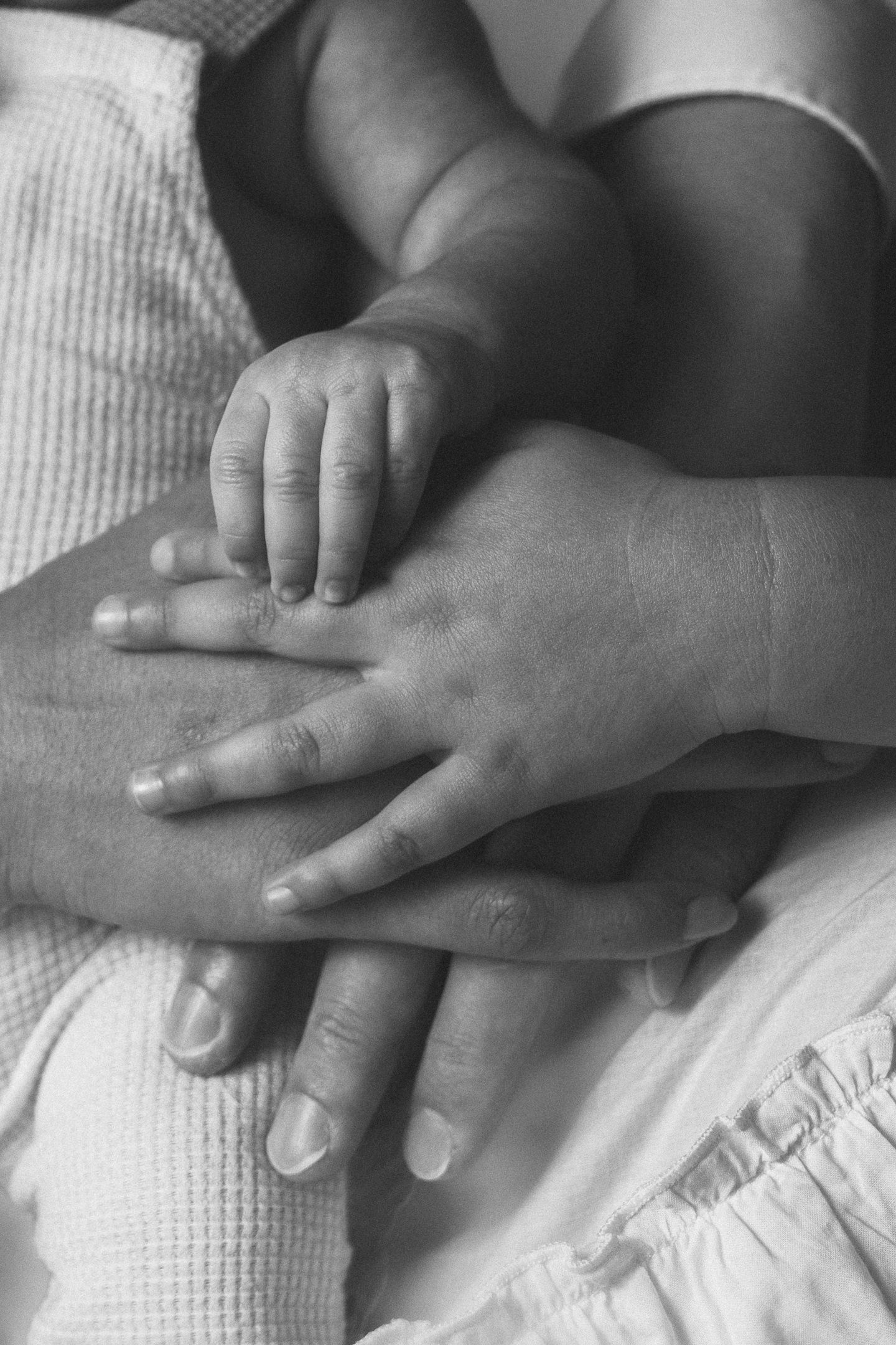 Close-up black and white image of tiny baby hands grasping against white fabric.