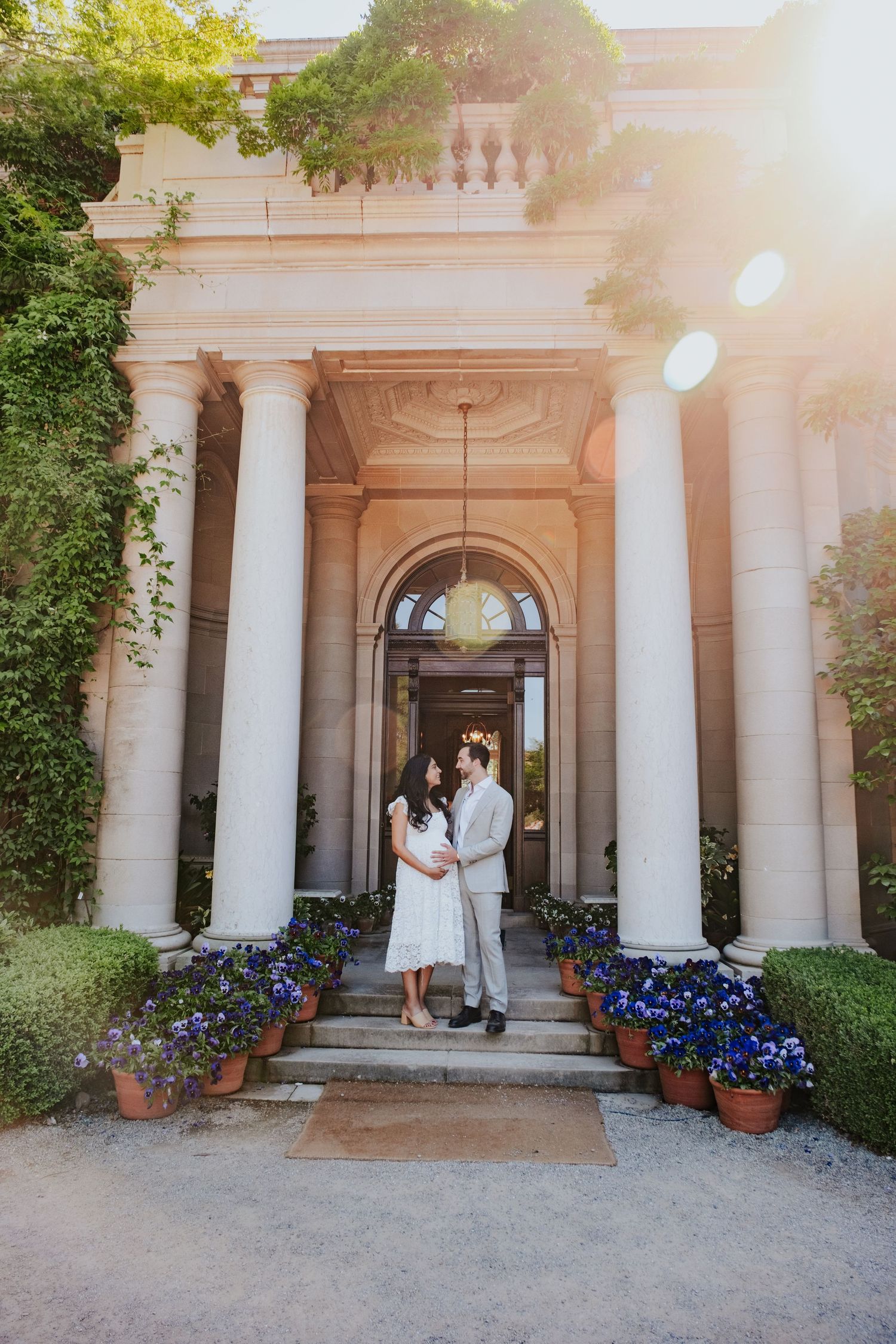 Elegant columned entrance with potted blue flowers and couple in white.