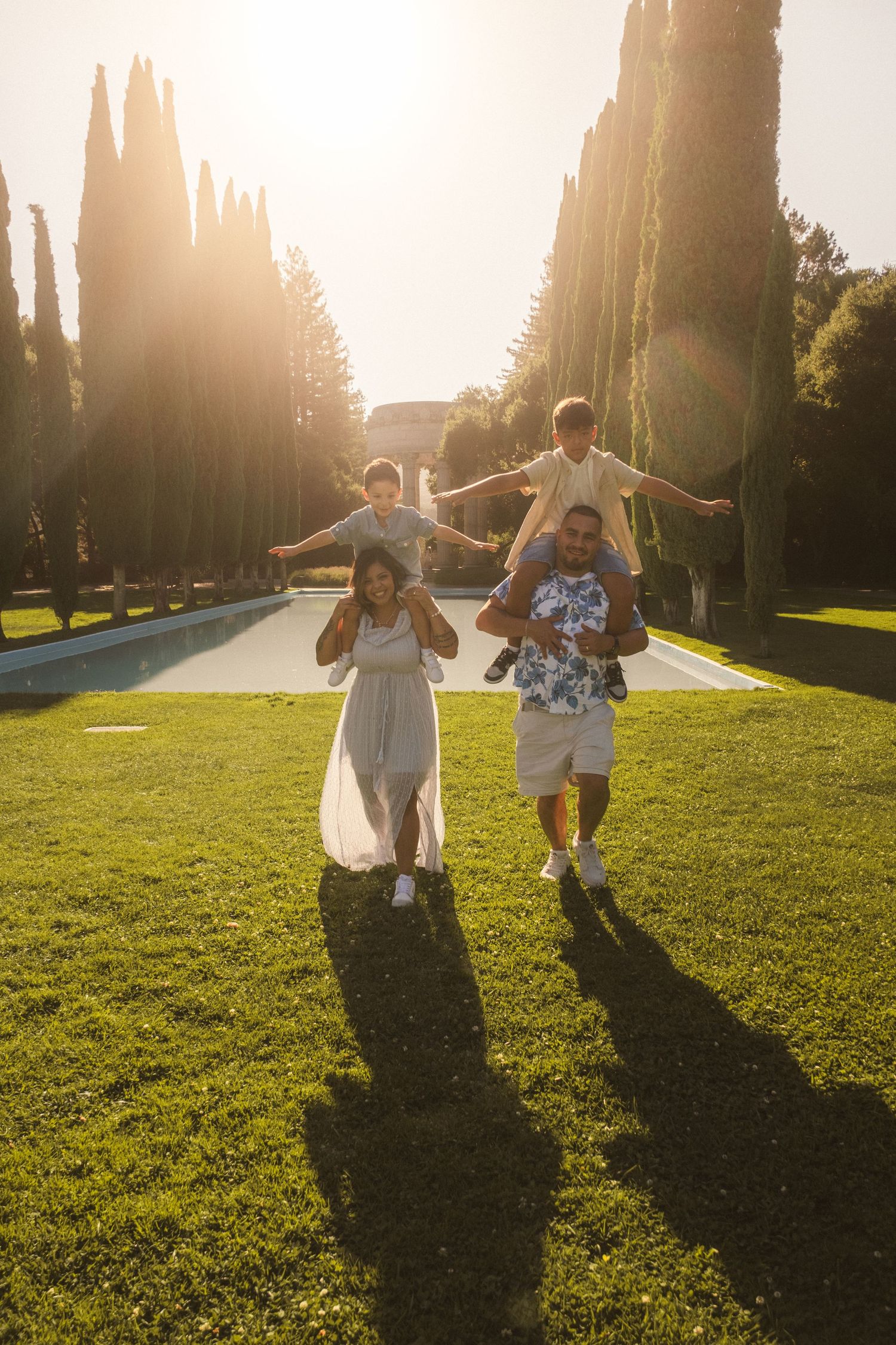 People run joyfully across a lawn with arms spread wide during sunset.