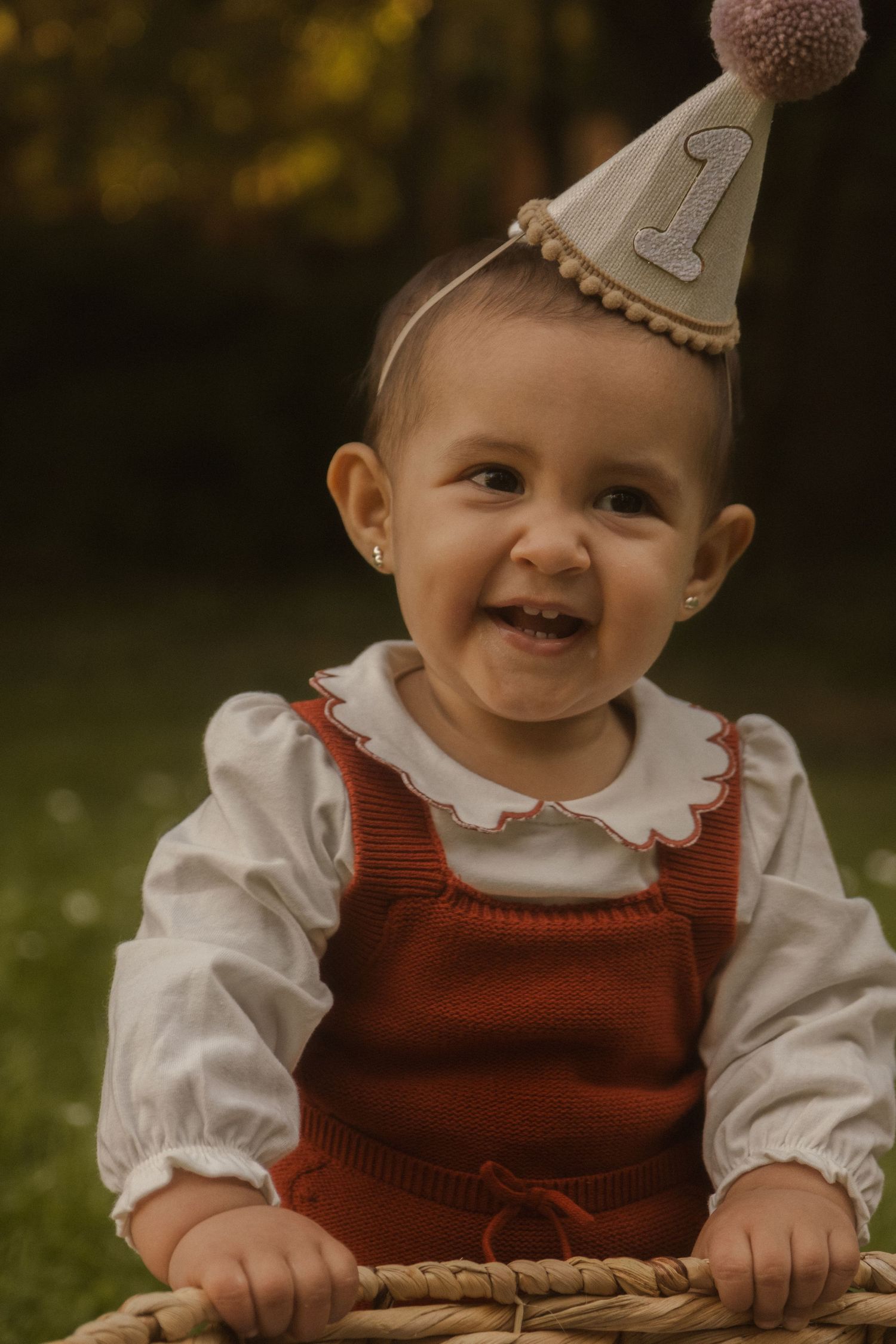 Baby wearing party hat and red outfit smiles during celebratory photoshoot.