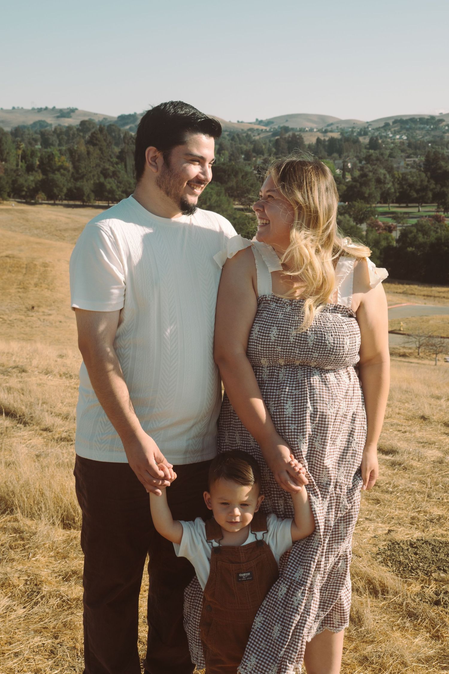 Family enjoying a casual outdoor photoshoot in rolling hills landscape.