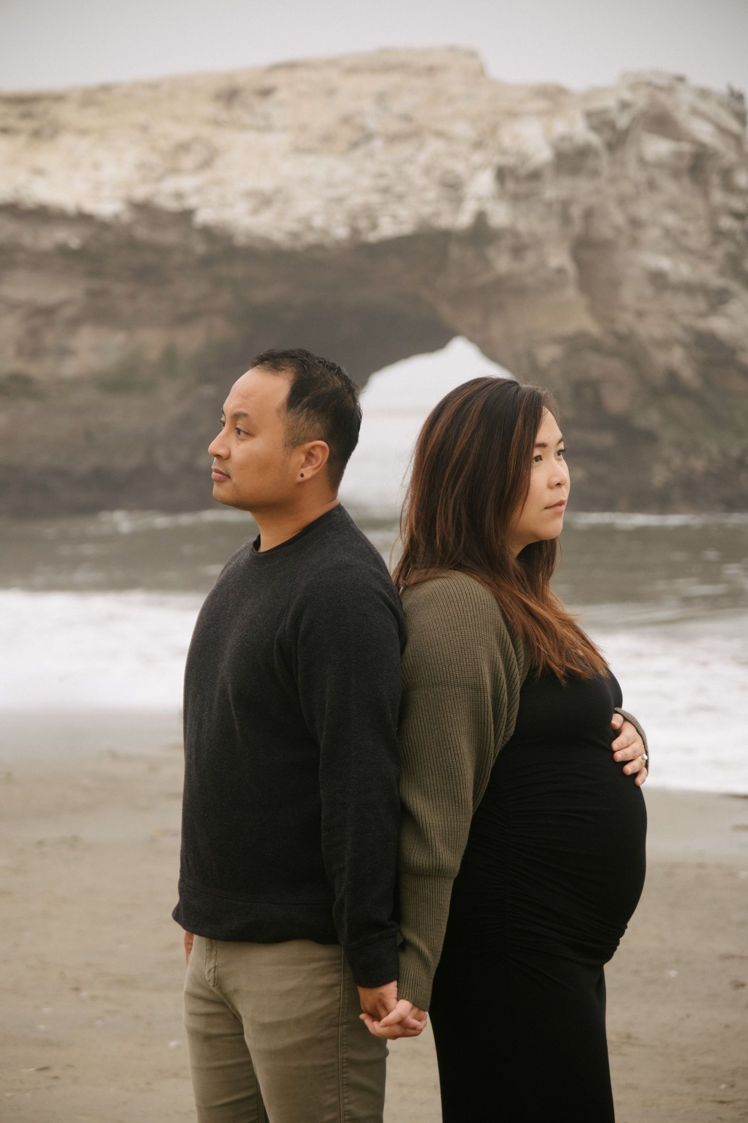 A couple embraces while standing on a rocky beach during an overcast day.