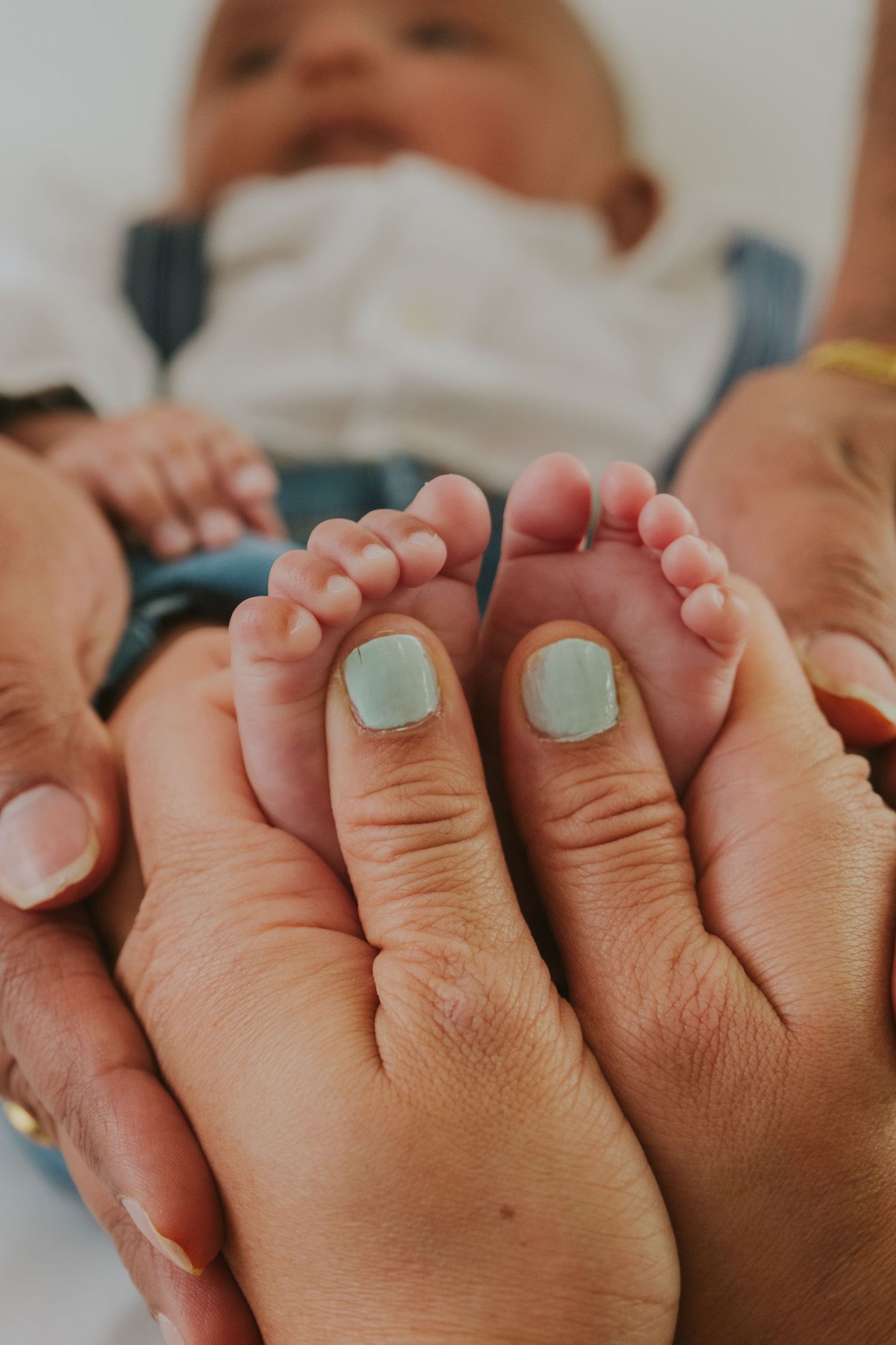 Adult hands holding tiny baby feet with painted teal toenails.