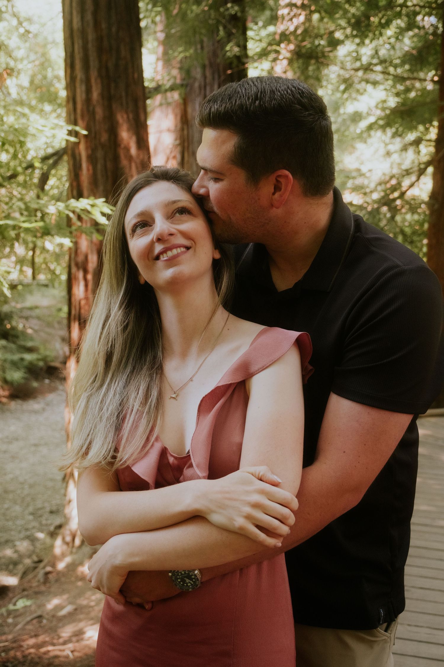A couple shares tender moments together on a forest path in warm sunlight.