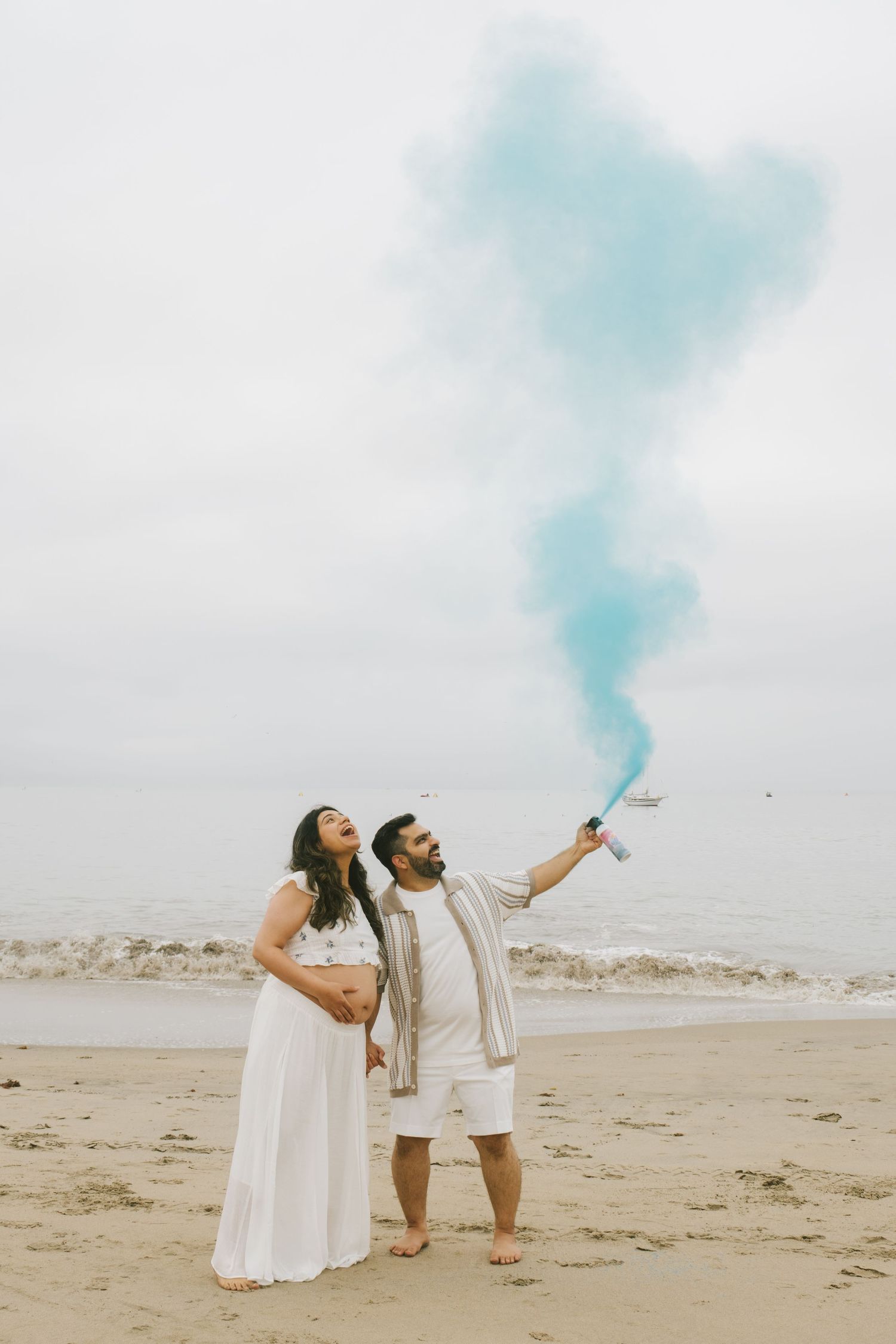 Couple celebrating on a beach with blue smoke bombs creating a dreamy atmosphere.