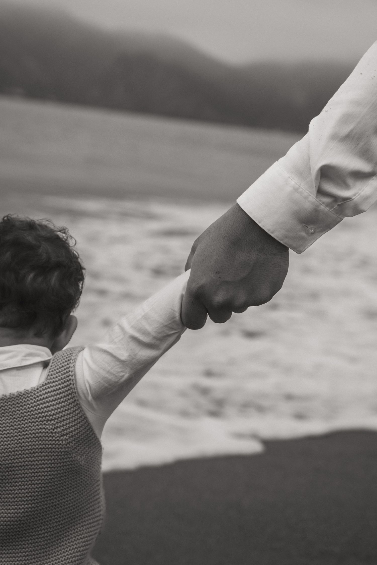 Close-up black and white shot of hands reaching toward ocean waves.