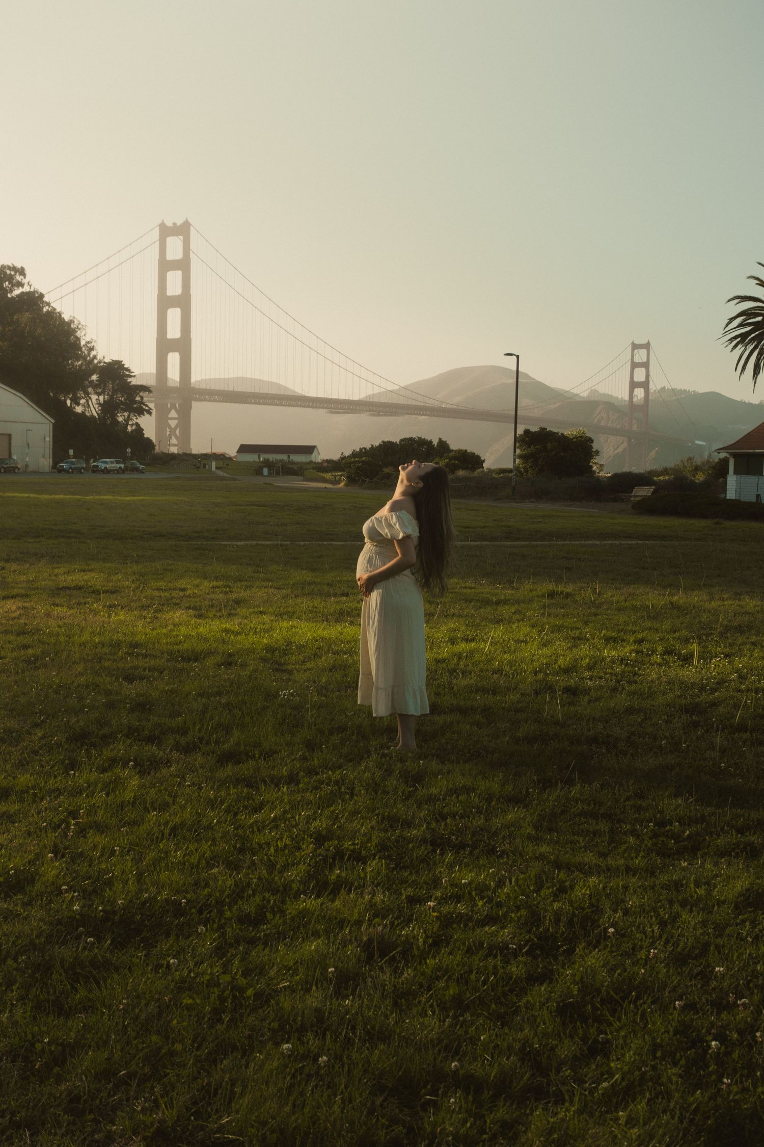 Grassy field with the Golden Gate Bridge visible in the background during sunset.