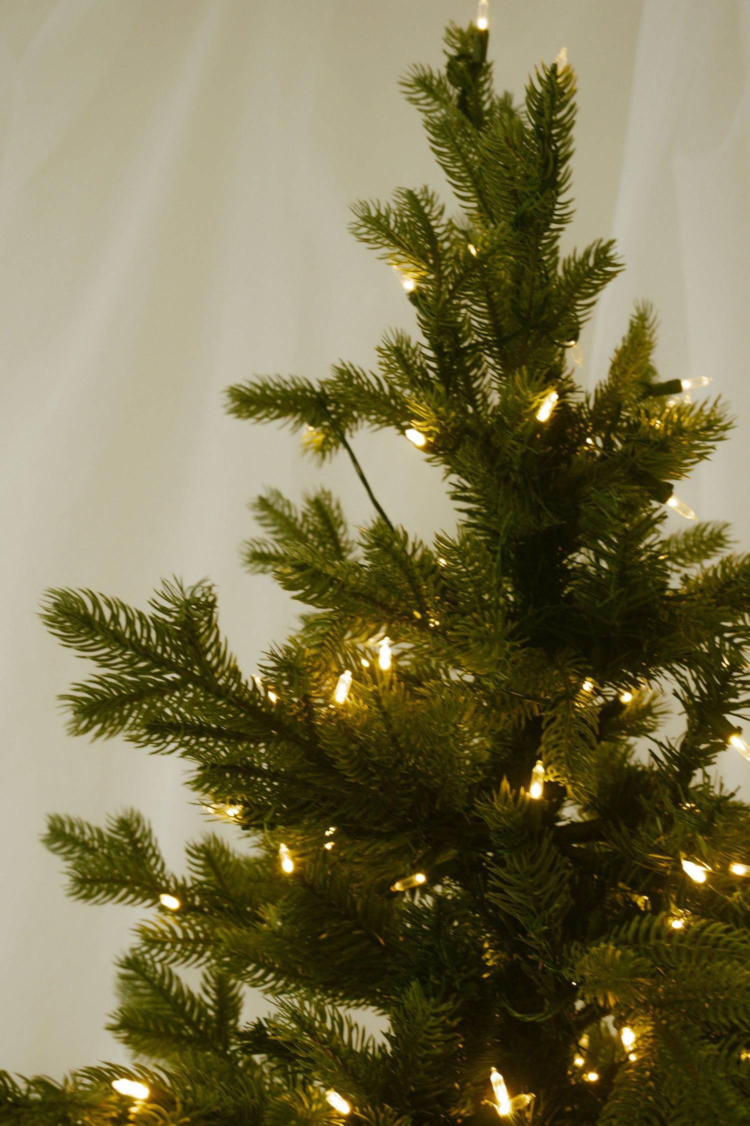 Close-up view of illuminated Christmas tree branches with warm white lights against a light background.